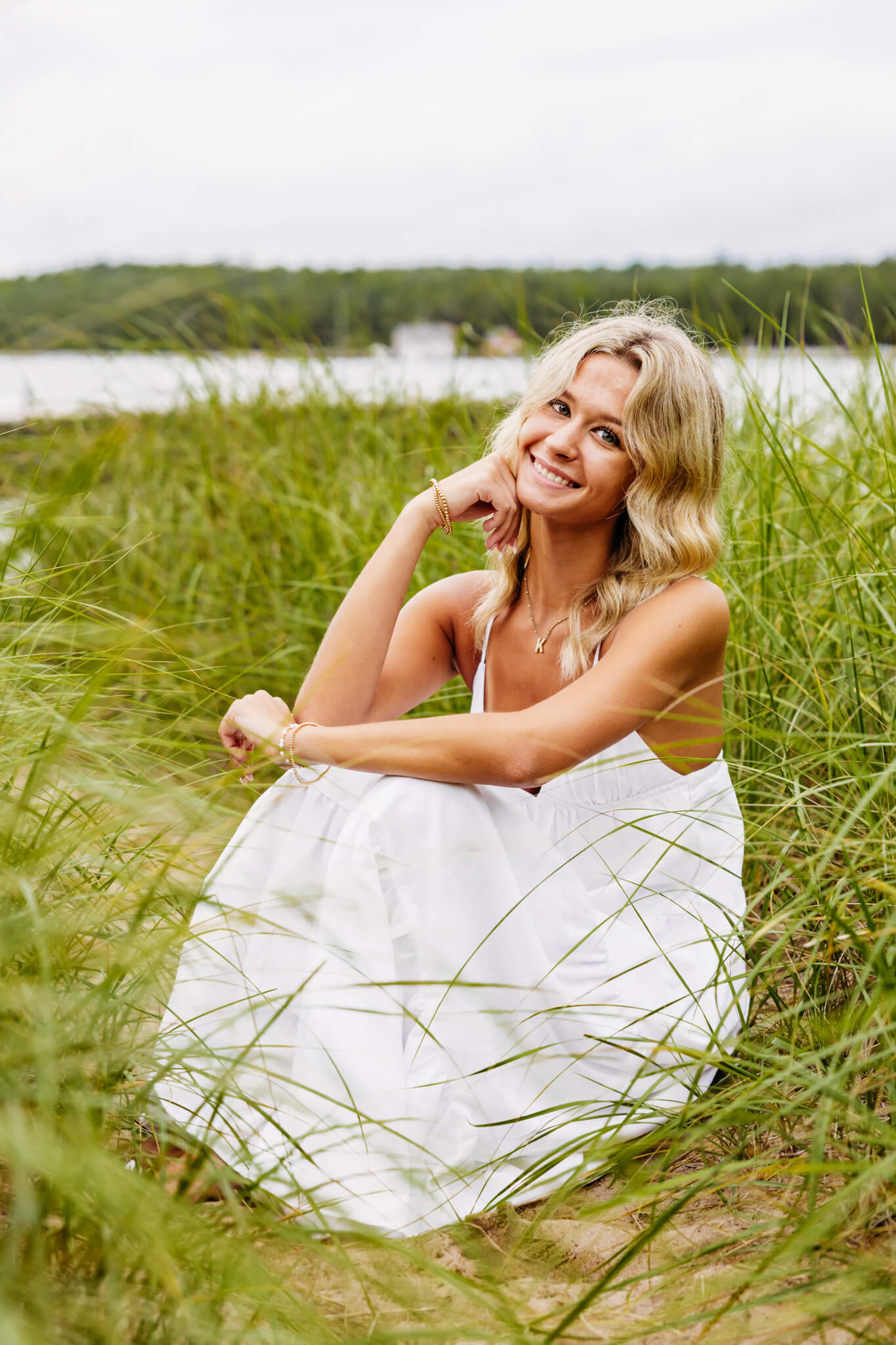 Blonde teen girl in a white flowy dress sitting on a beach in Egg Harbor.