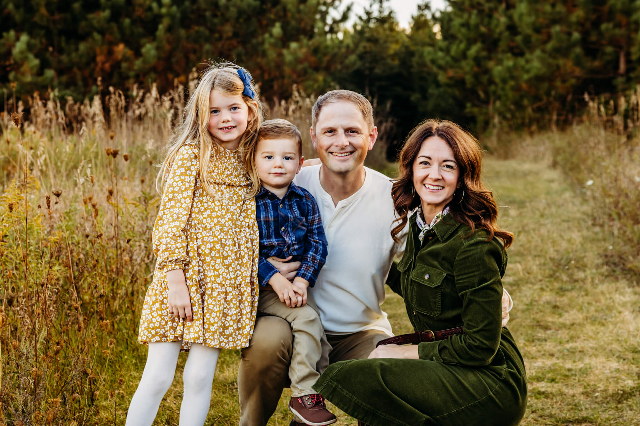 Beautiful family of four kneeling in a grassy path at a park near Milwaukee Wi