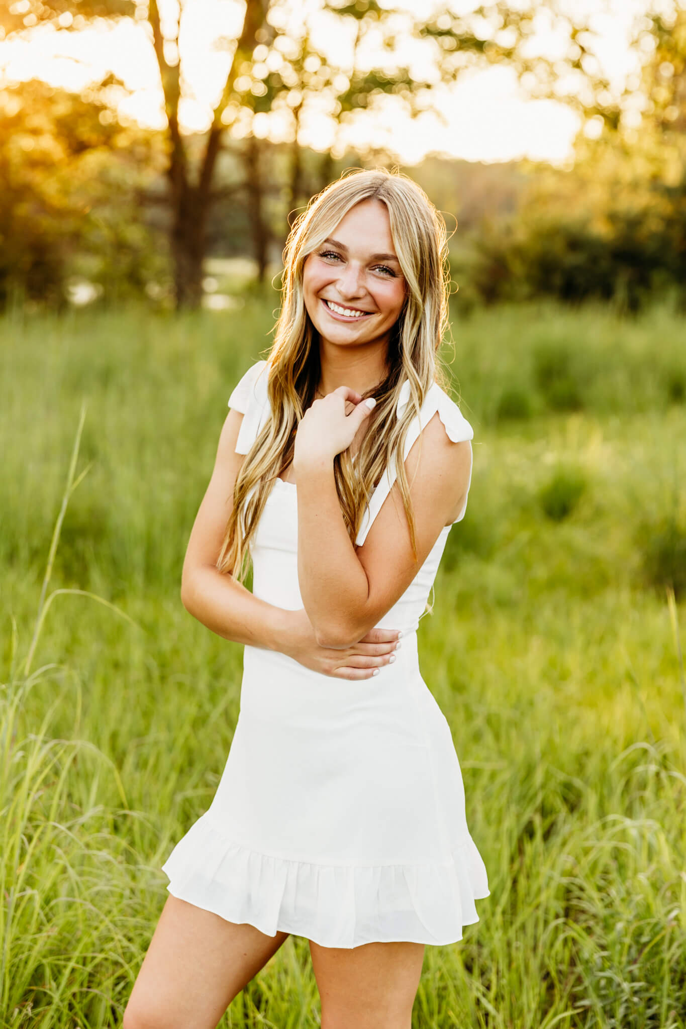 high school senior in a short white dress standing in a grassy field at sunset as she plays with her hair for a blog post about volunteer opportunities in Green Bay