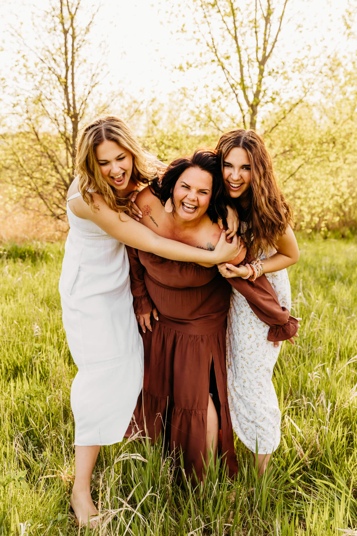 two teenage daughters laughing as they hug their mama from behind in a field near Appleton