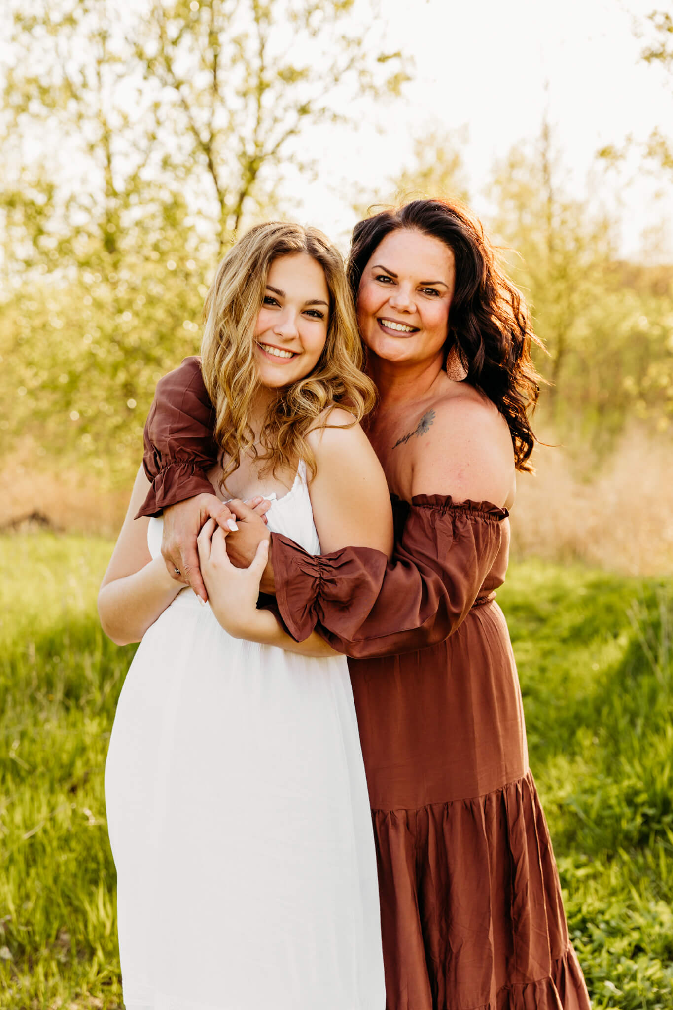 beautiful brunette mom in a brown dress hugging her teen daughter from behind in a white dress for a blog post about New Fusion Dance in Appleton