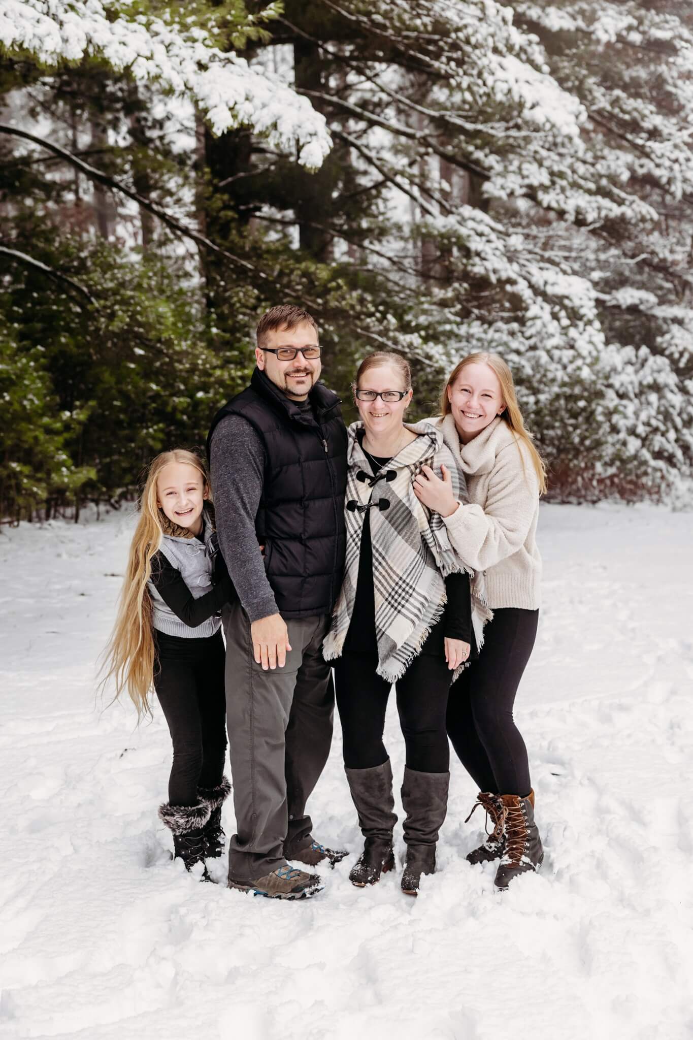 mother and father playing with their two teen daughters on a snowy day at Aissen Tree Farm