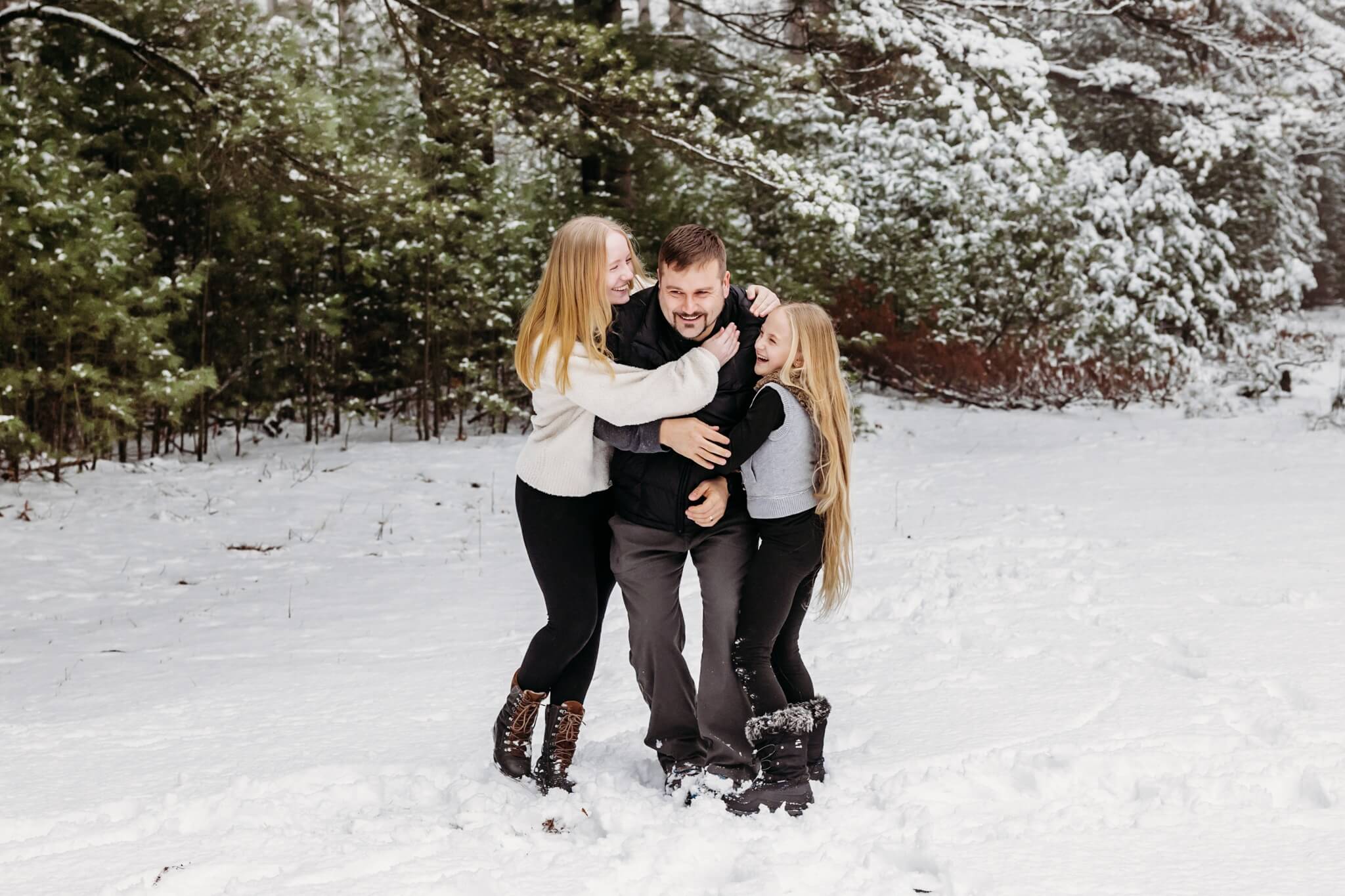 Dad being hugged by both of his daughters while they play in the snow.