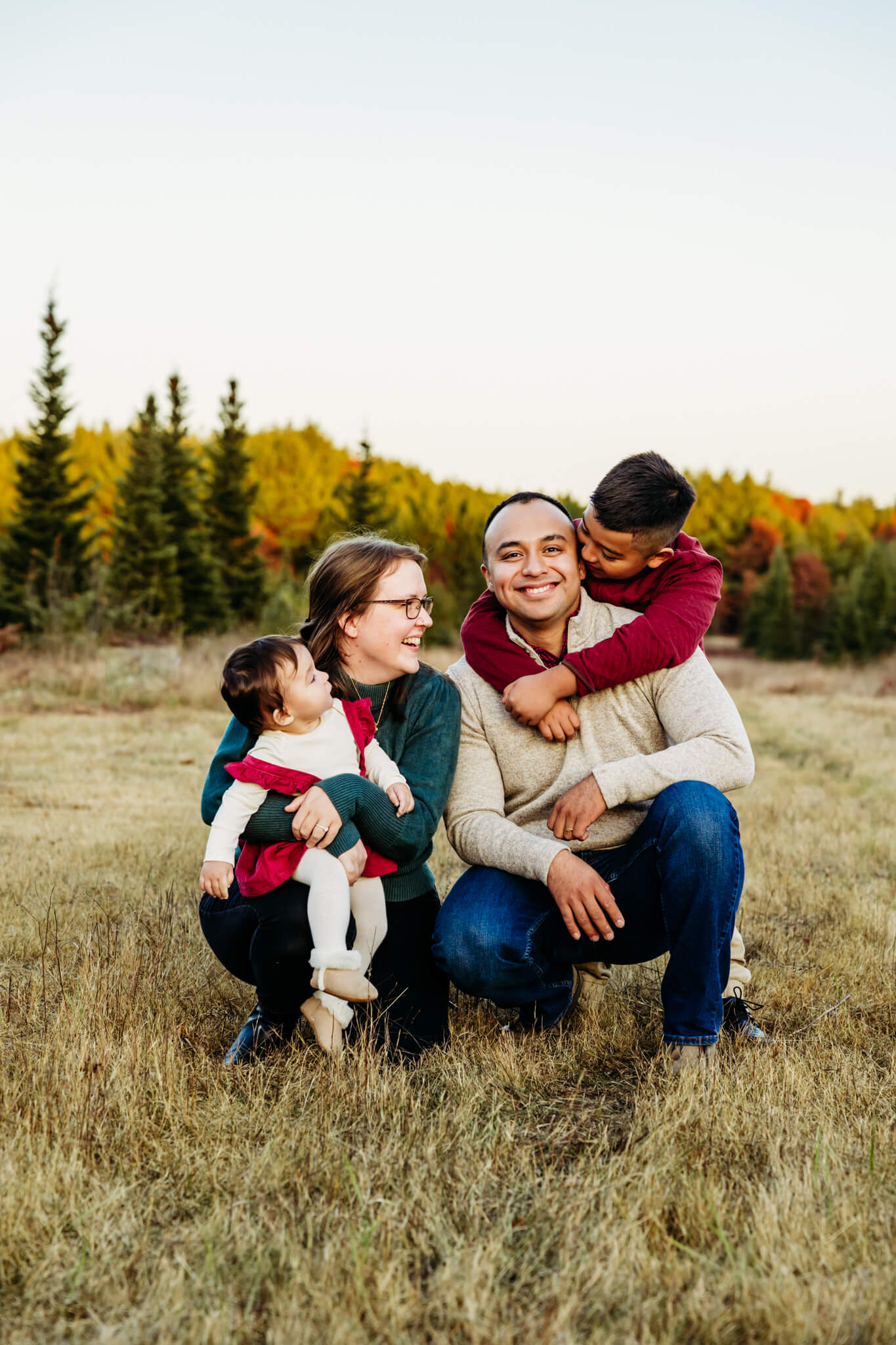 Family of four laughing together as they kneel down on the ground while enjoying their Christmas Mini session.