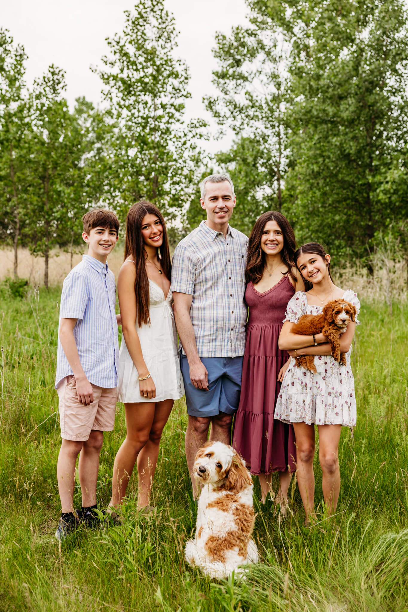 Adorable family of five standing in a spring field with their dog and puppy for a blog about hydrafacials in Appleton Wi.