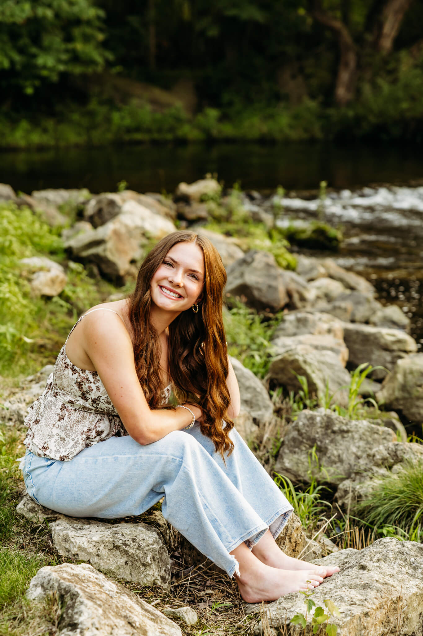 Gorgeous teen girl sitting on the rocks along a river creek for her senior photos.