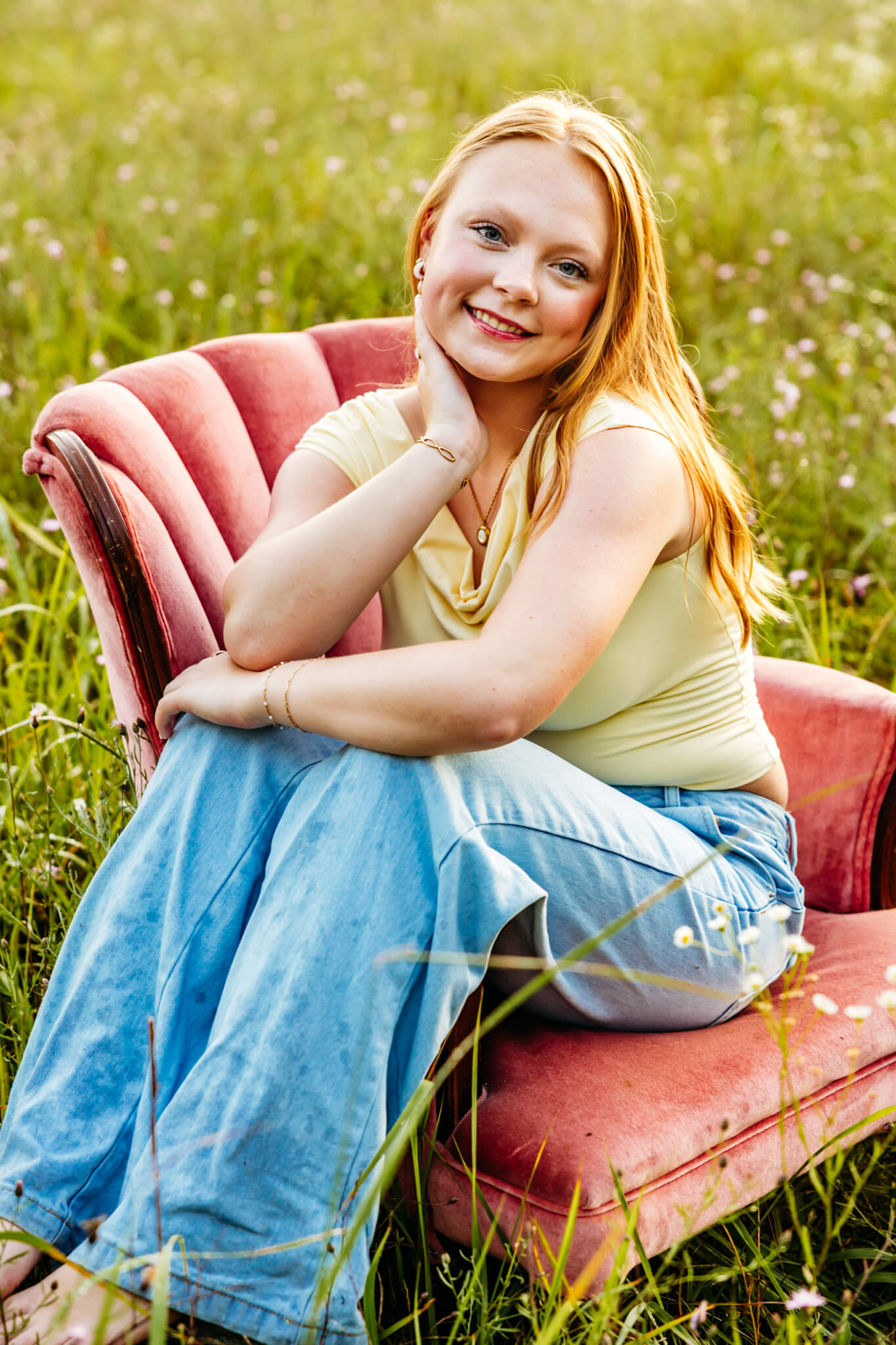 Ripon High School senior sitting on a pink velvet chair with her legs over the arm as she poses for her senior photos.