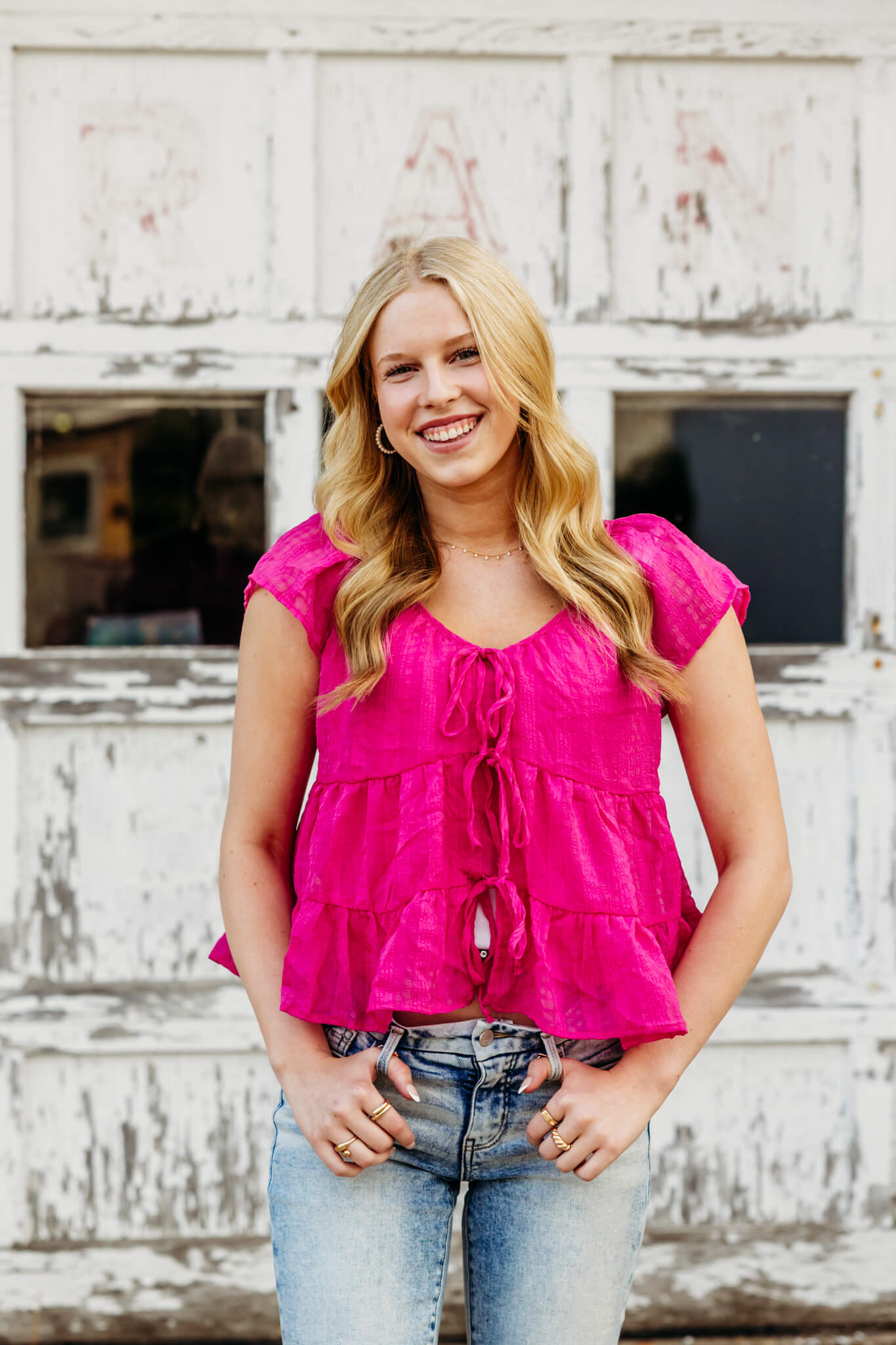 Young lady in a pink top and jeans laughing as she stands in front of a white garage door near Menasha.