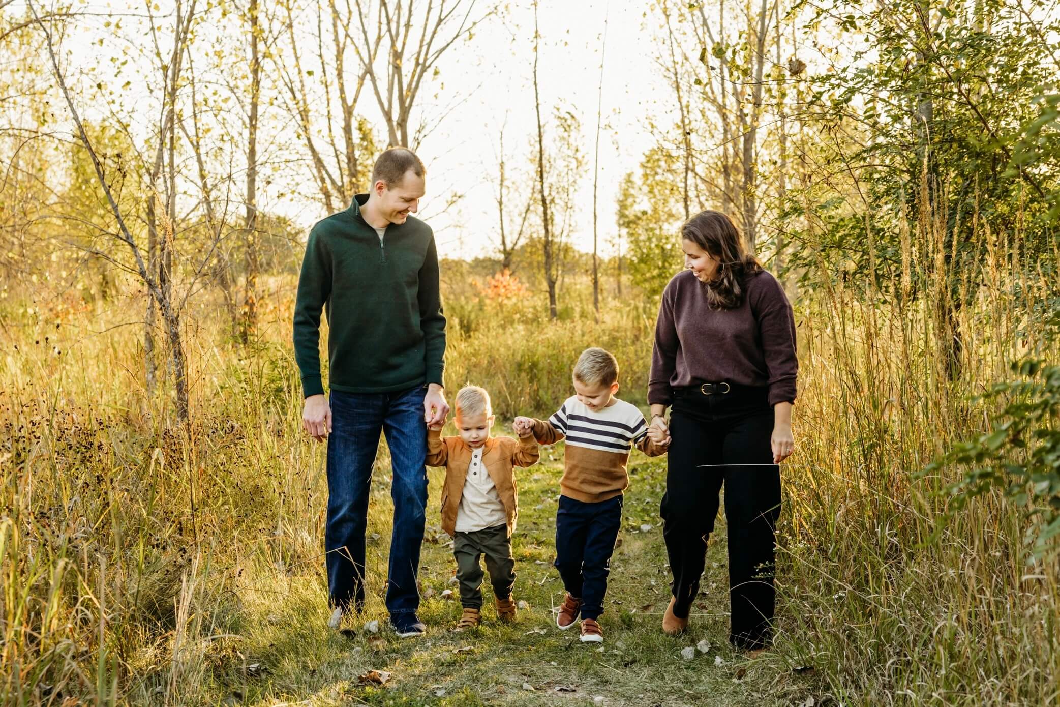 Mother and father walking with their two young boys in a fall field at a pumpkin patch in Appleton WI