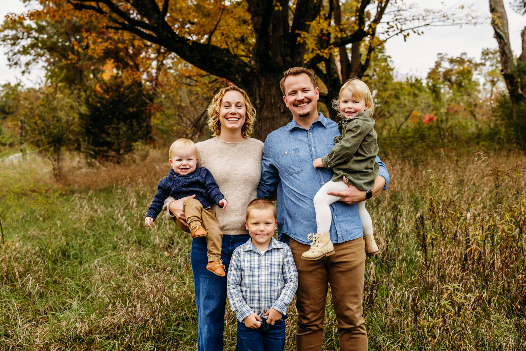 Family of 5 standing in a fall field and smiling for a blog post about pumpkin patches in Oshkosh WI