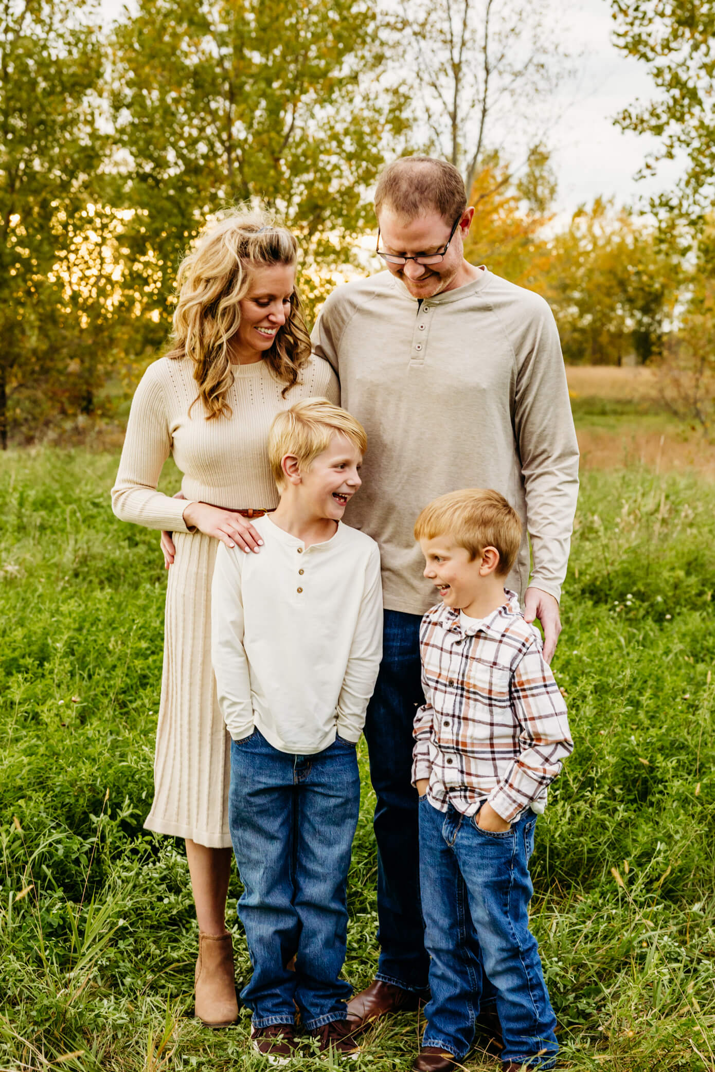 Family of four dressed in cream outfits laughing with each other during their family session.