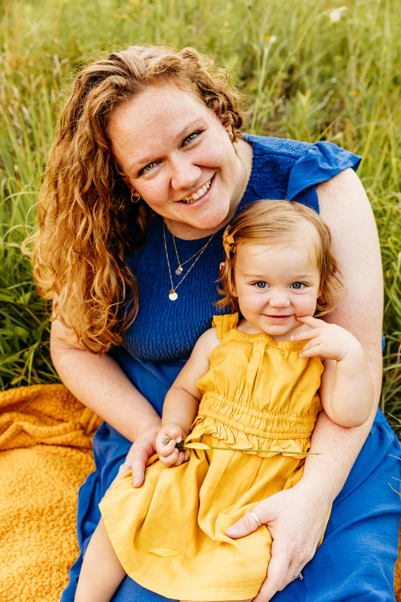 beautiful mama in a blue dress holding her baby girl in a yellow dress.