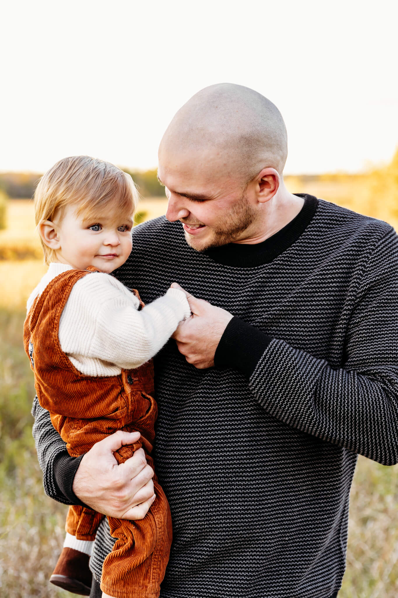 dad holding his 1 year old son as they laugh together while standing in a grassy field