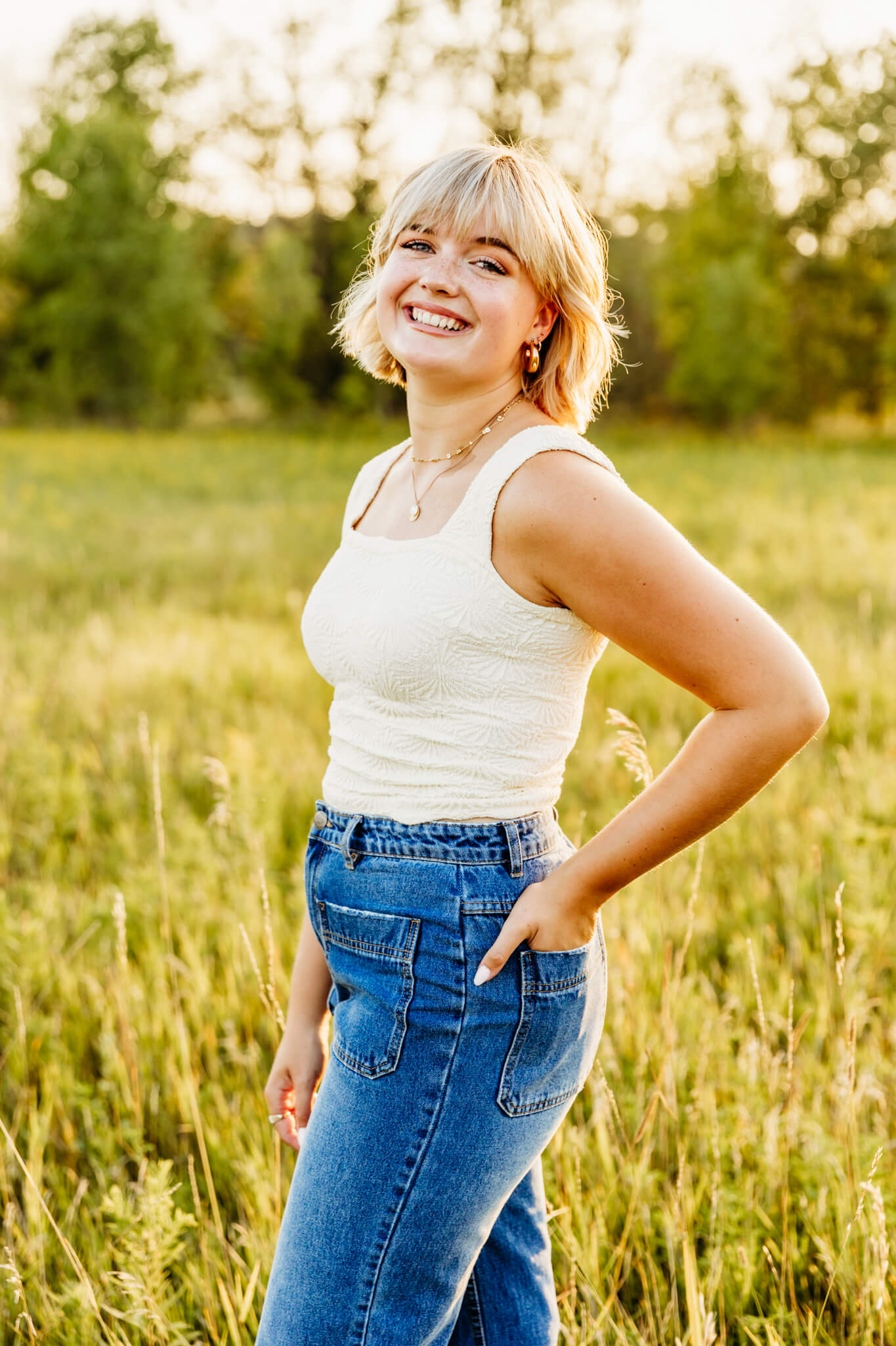 teen girl in a white tank top and jeans standing in a field smiling for a blog post about nail salons in appleton wi