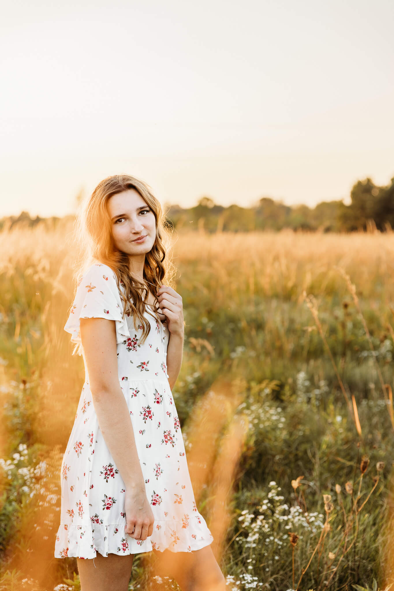 high school girl in a white dress standing in a grassy field at golden hour for blog post about universities in wisconsin