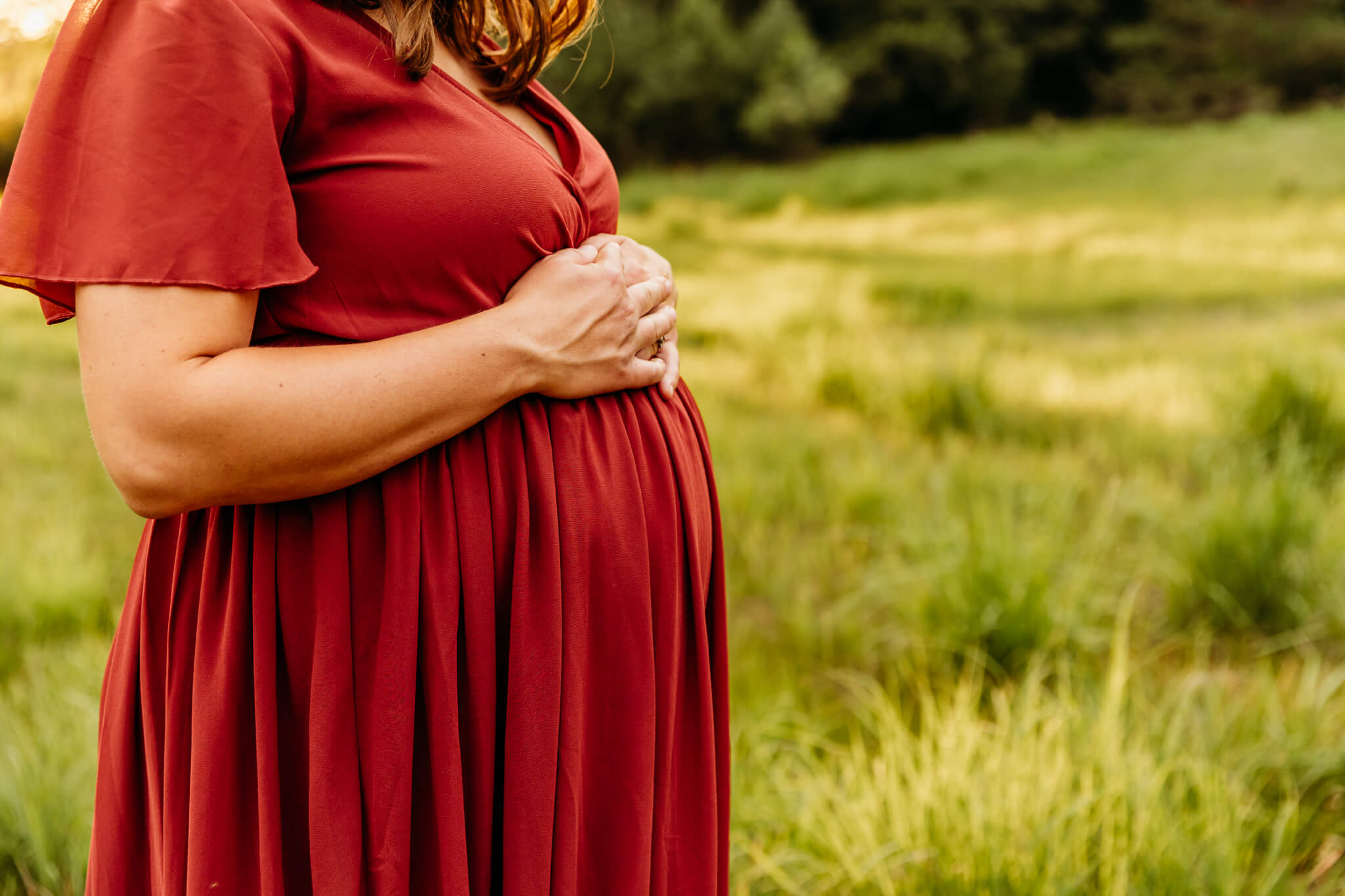 mom to be in a red dress resting hands on her baby bump in a field near Appleton