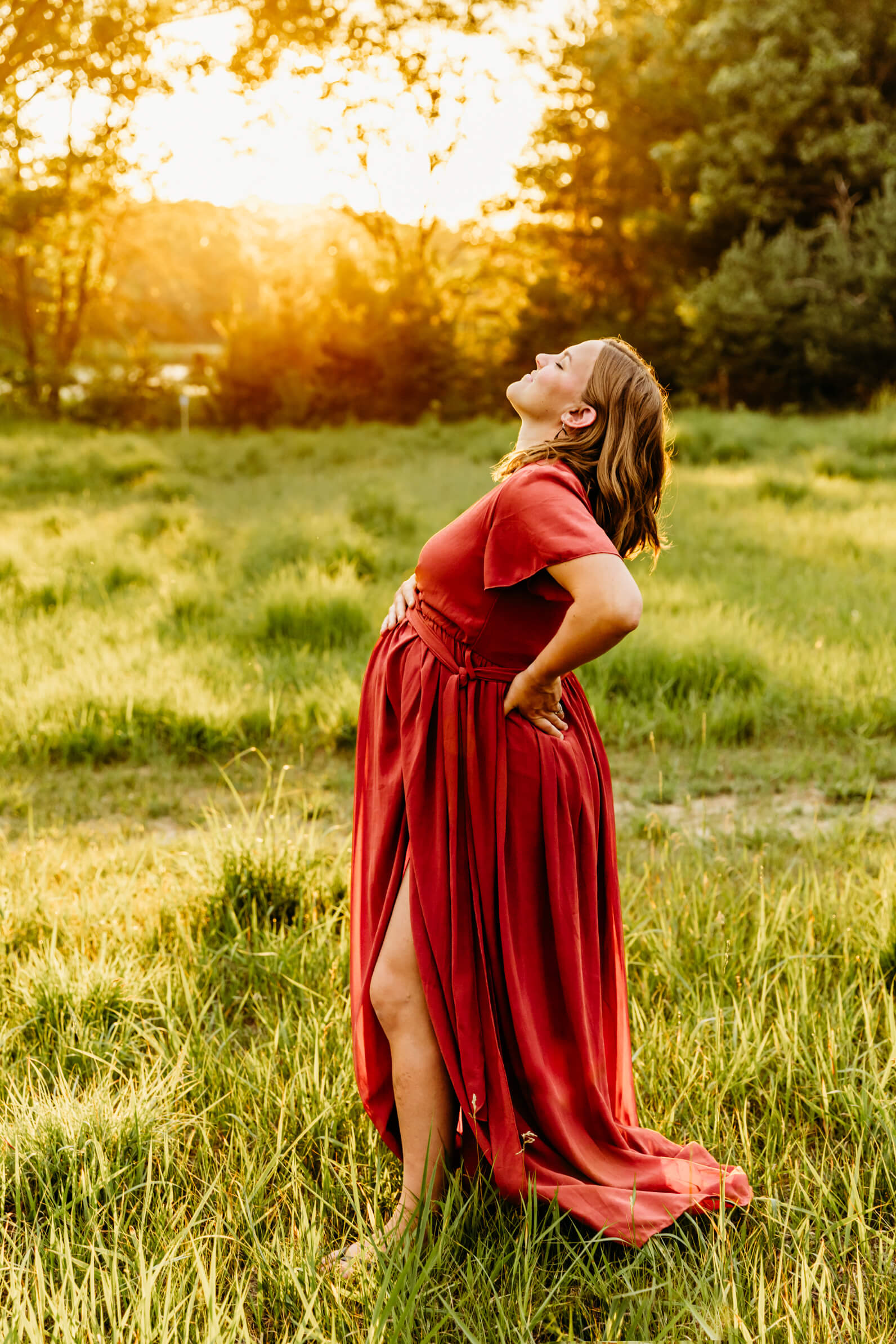 mom to be in a red dress putting her head back as she takes a deep breath in and lifts her chin up to the sky for blog post about Spas in Appleton