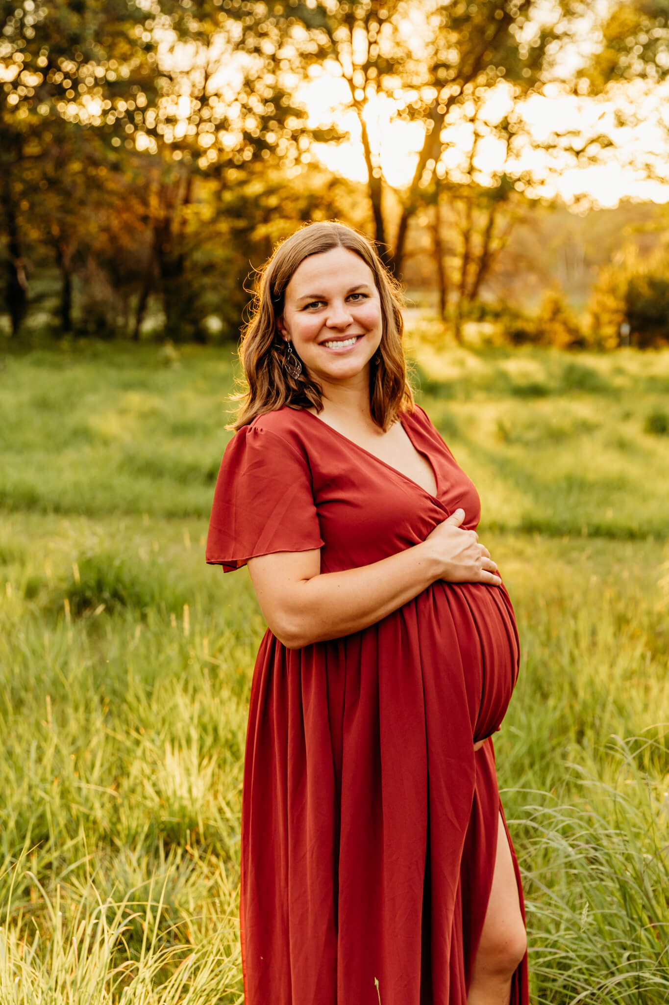 beautiful mom to be holding her baby bump in a glowing field as she smiles fiercely during her maternity session
