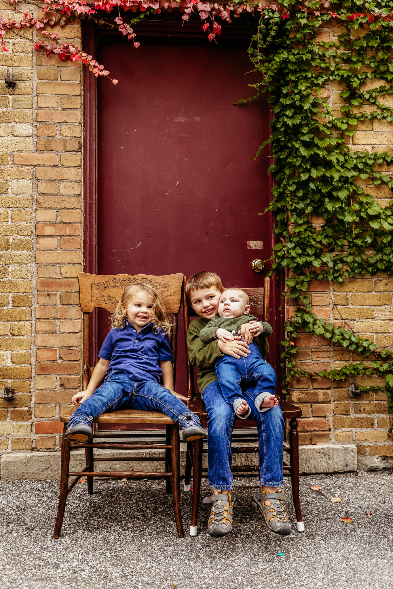 3 young brother sitting on wooden chairs in front of burgundy door