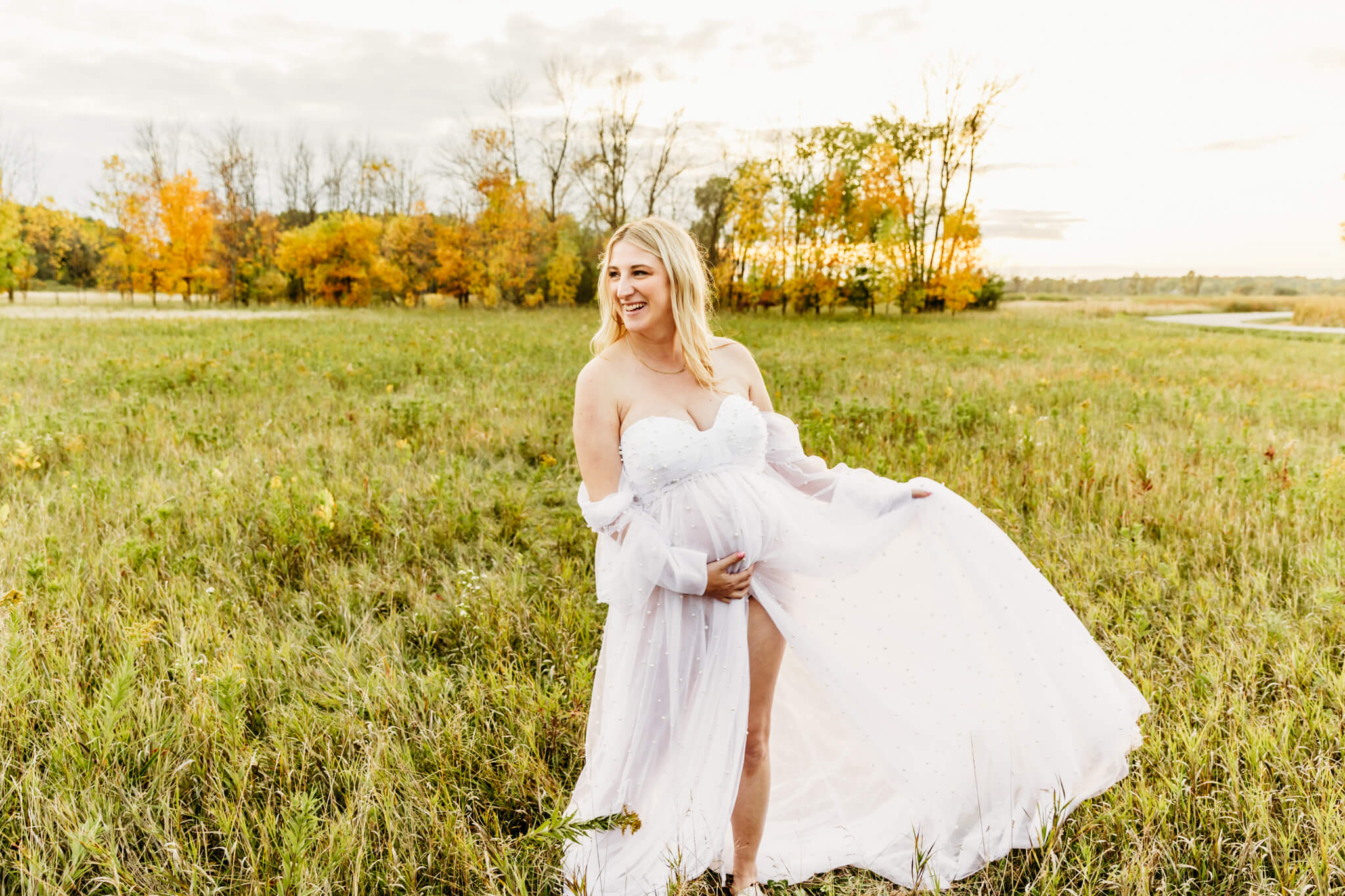 pregnant woman dancing in her white gown in a field at sunset