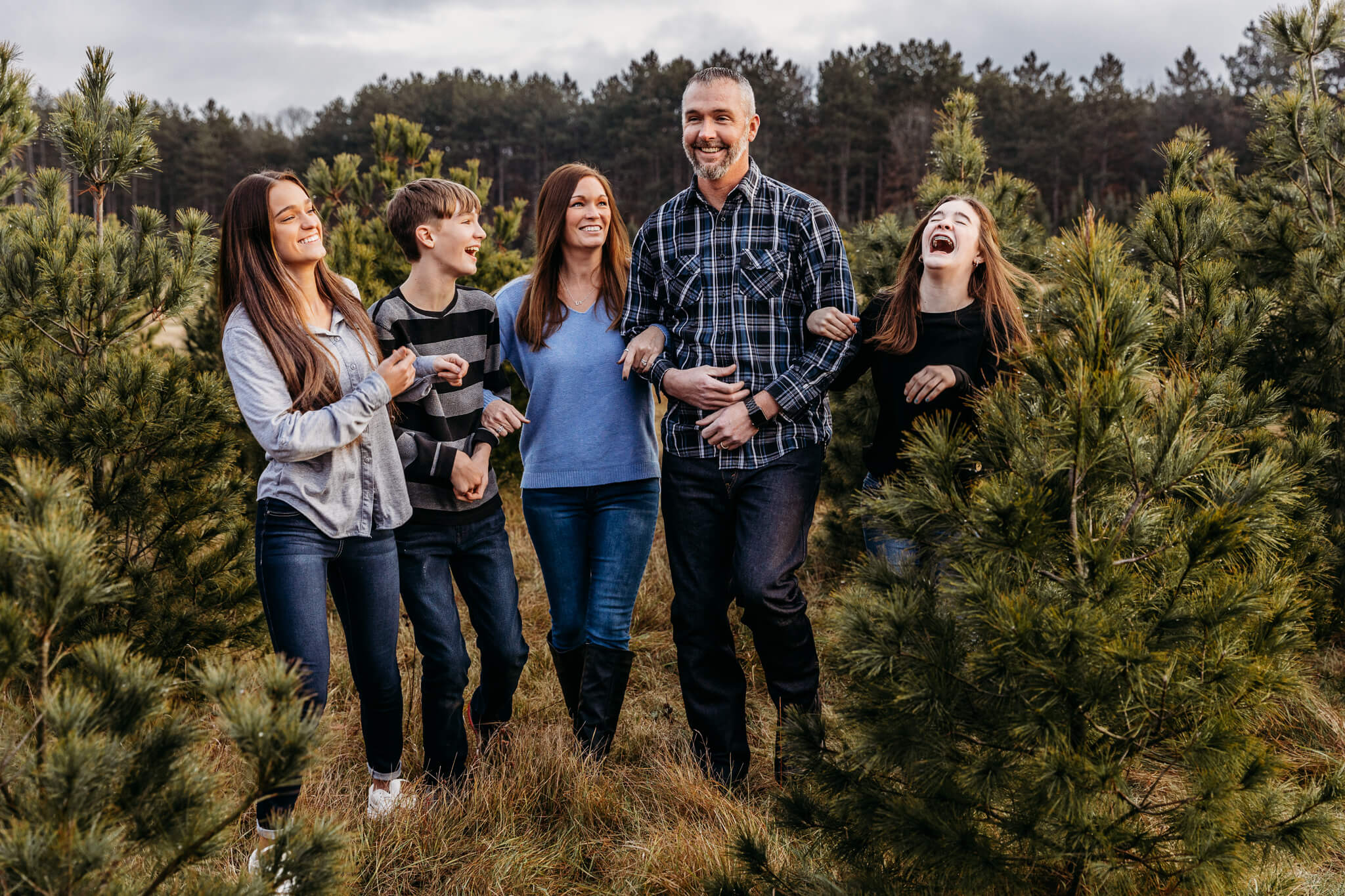 family walking through pine trees together for family session by Ashley Kalbus