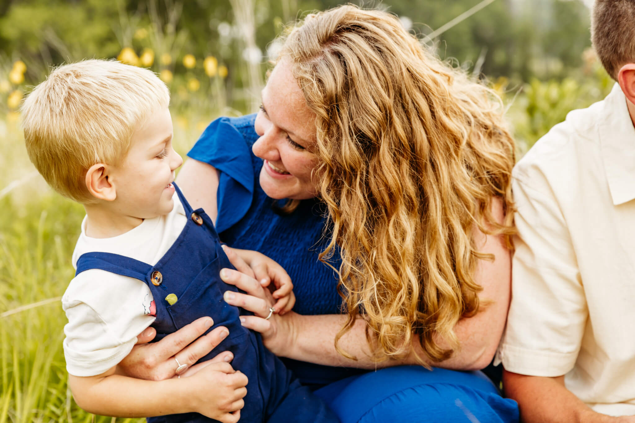mama in blue dress tickling her son in blue overalls as they laugh together