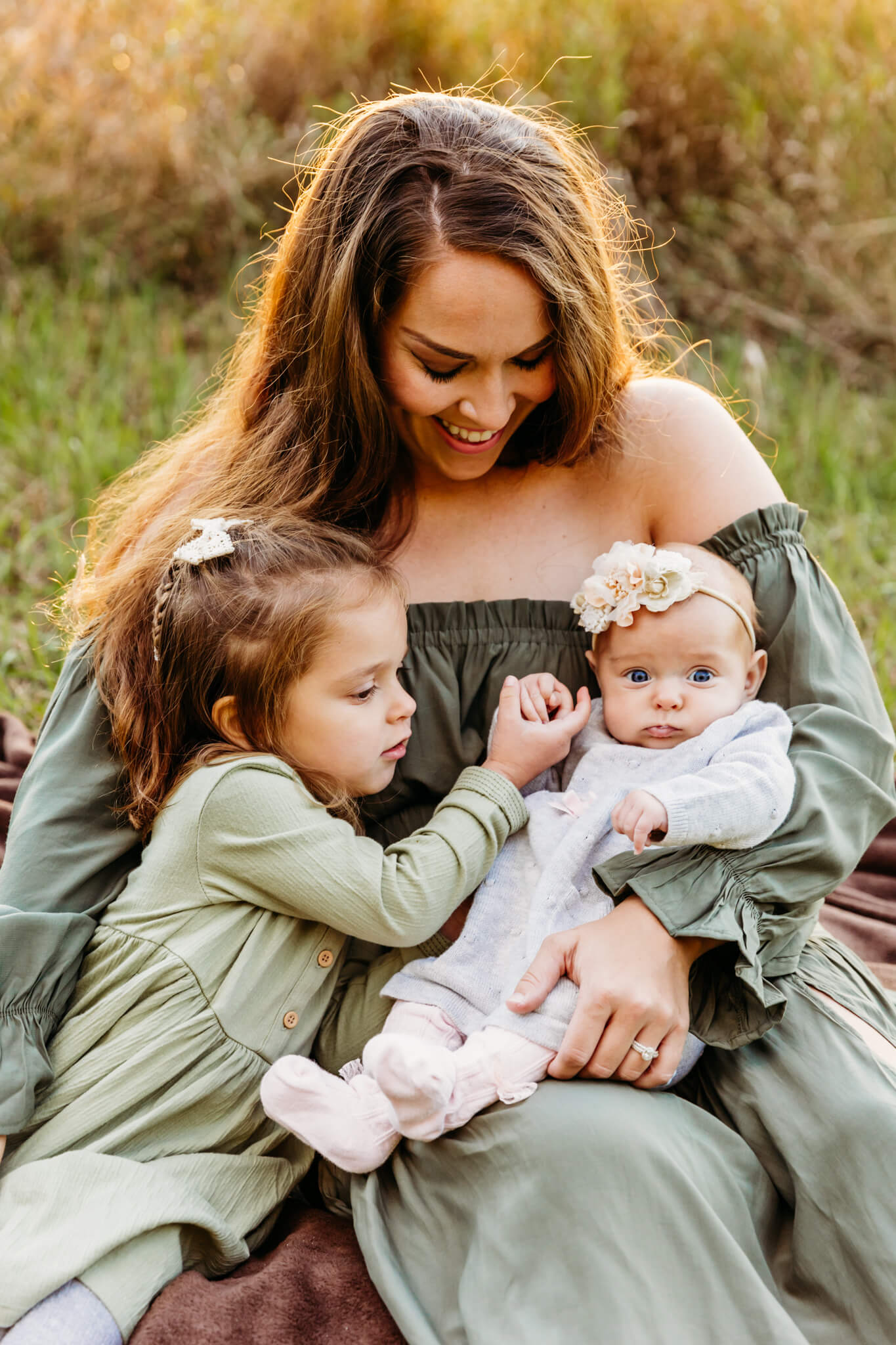 mama snuggling her two daughters as her toddler holds her baby's hand