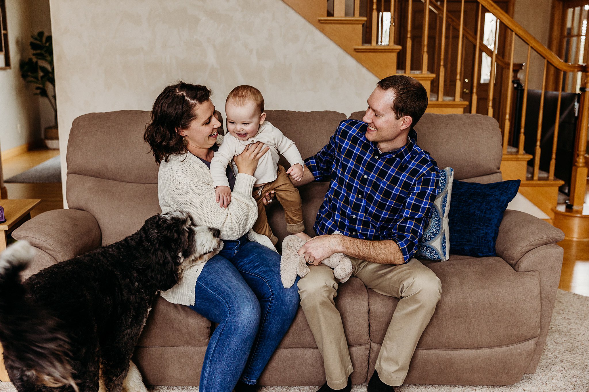 new family of three sitting on a couch in their home with their dog