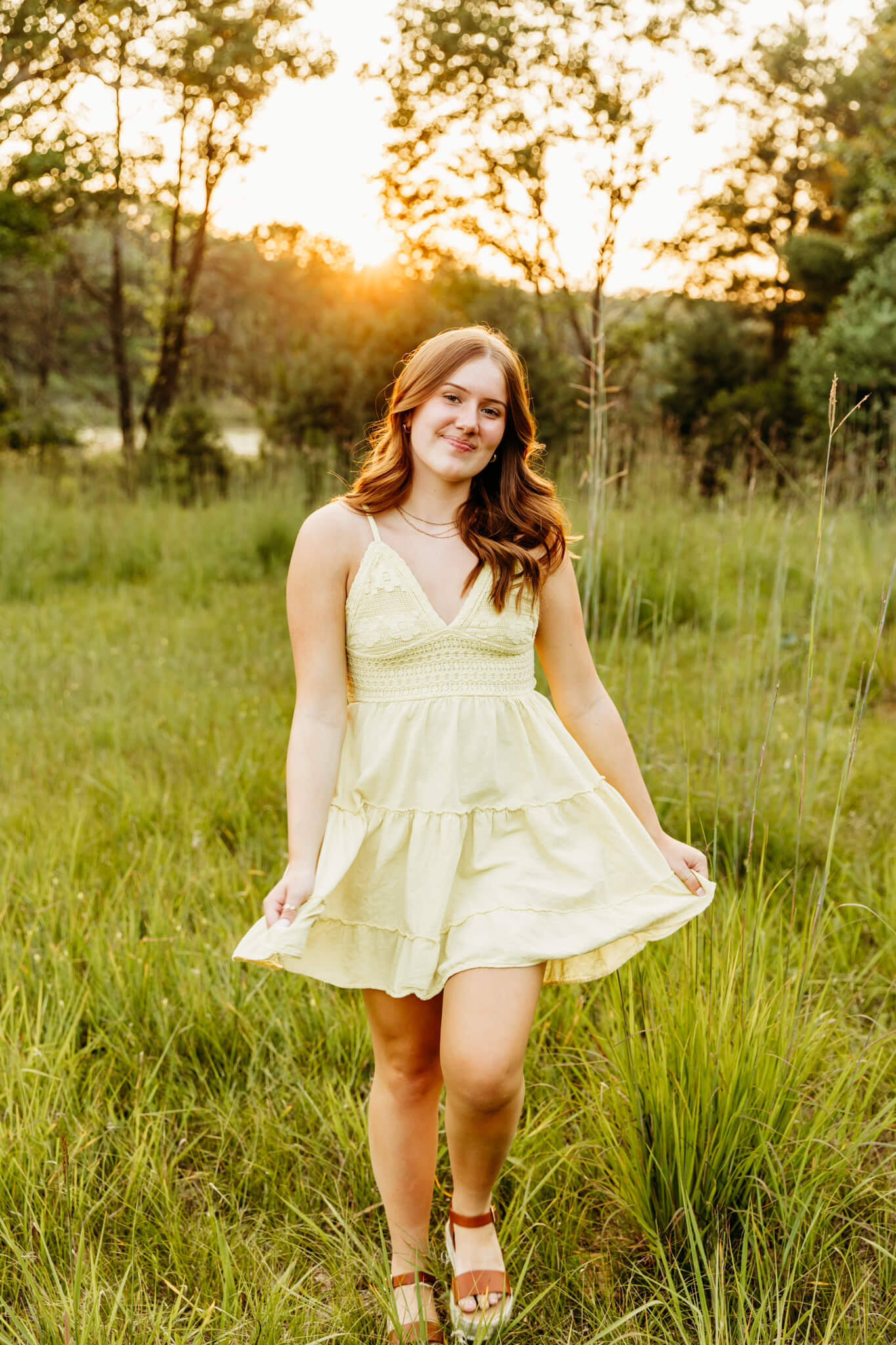 teen girl in a yellow dress walking through a grassy field at sunset for a blog post about Milwaukee Hair Salons