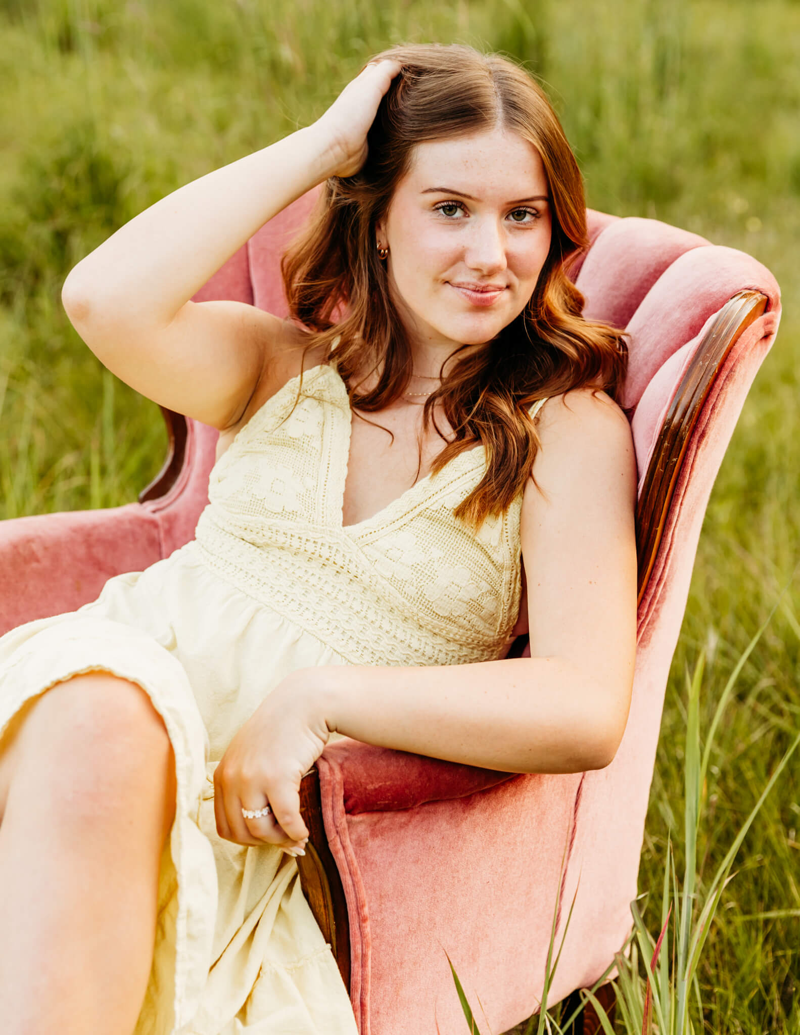 gorgeous teenage girl pulling her hair back as she sits in a pink chair during her senior photo session