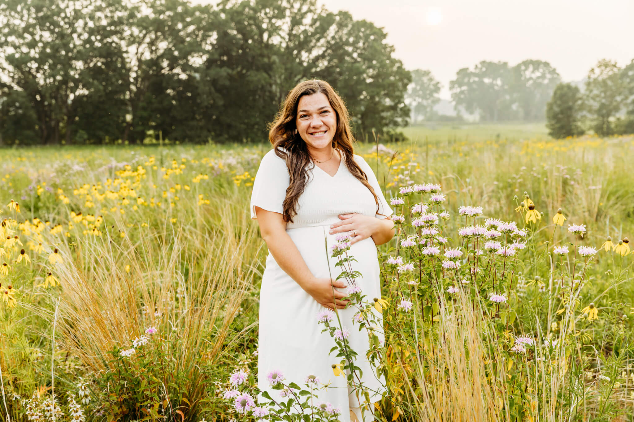 gorgeous mama to be holding her baby bump in a field of wildflowers