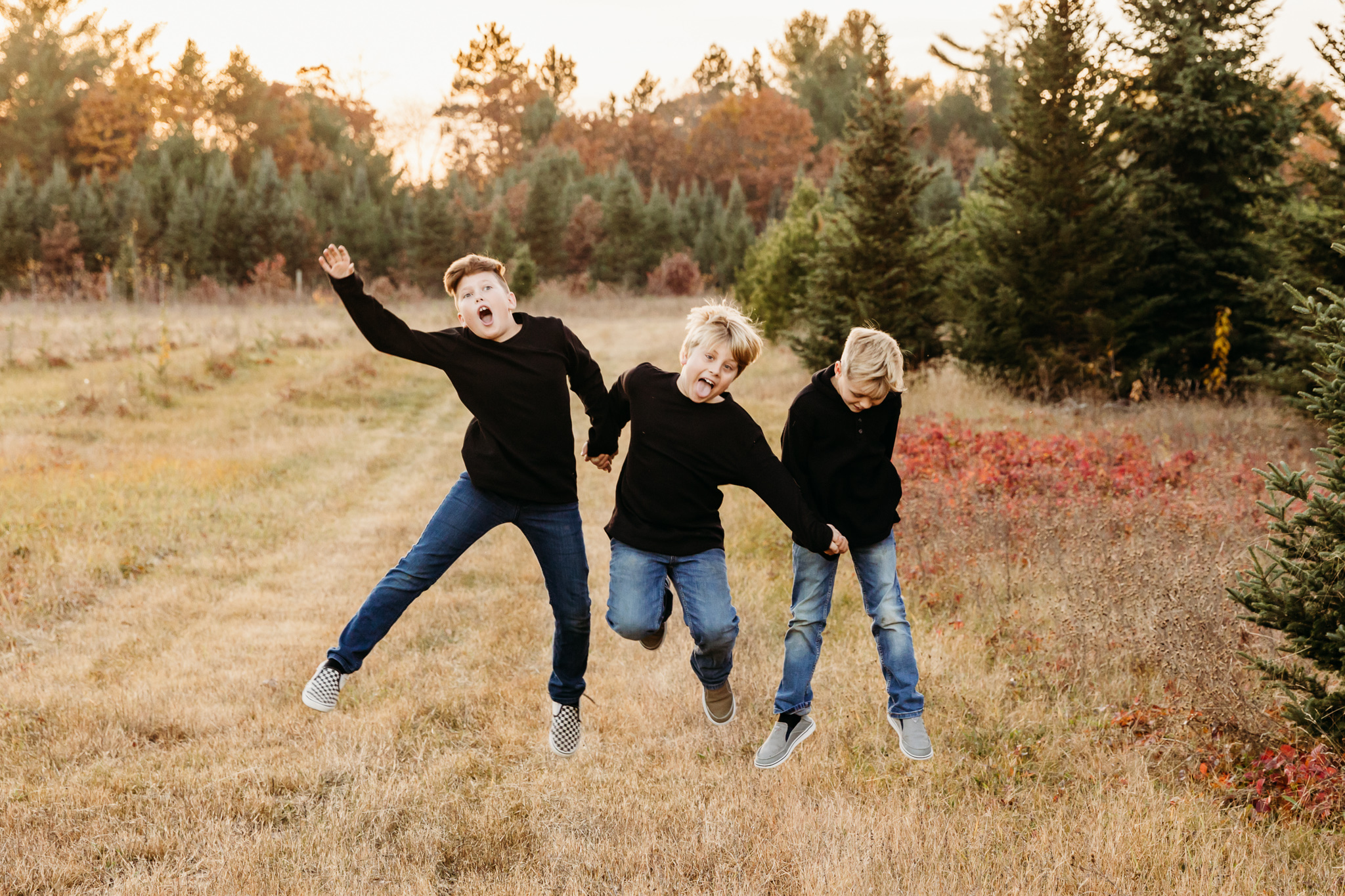 3 brothers wearing black shirts and jeans jumping in a field near milwaukee