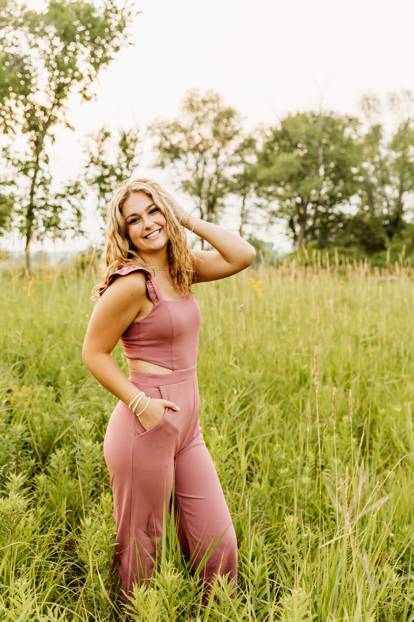 beautiful high school girl in a pink jumpsuit standing in a grassy field