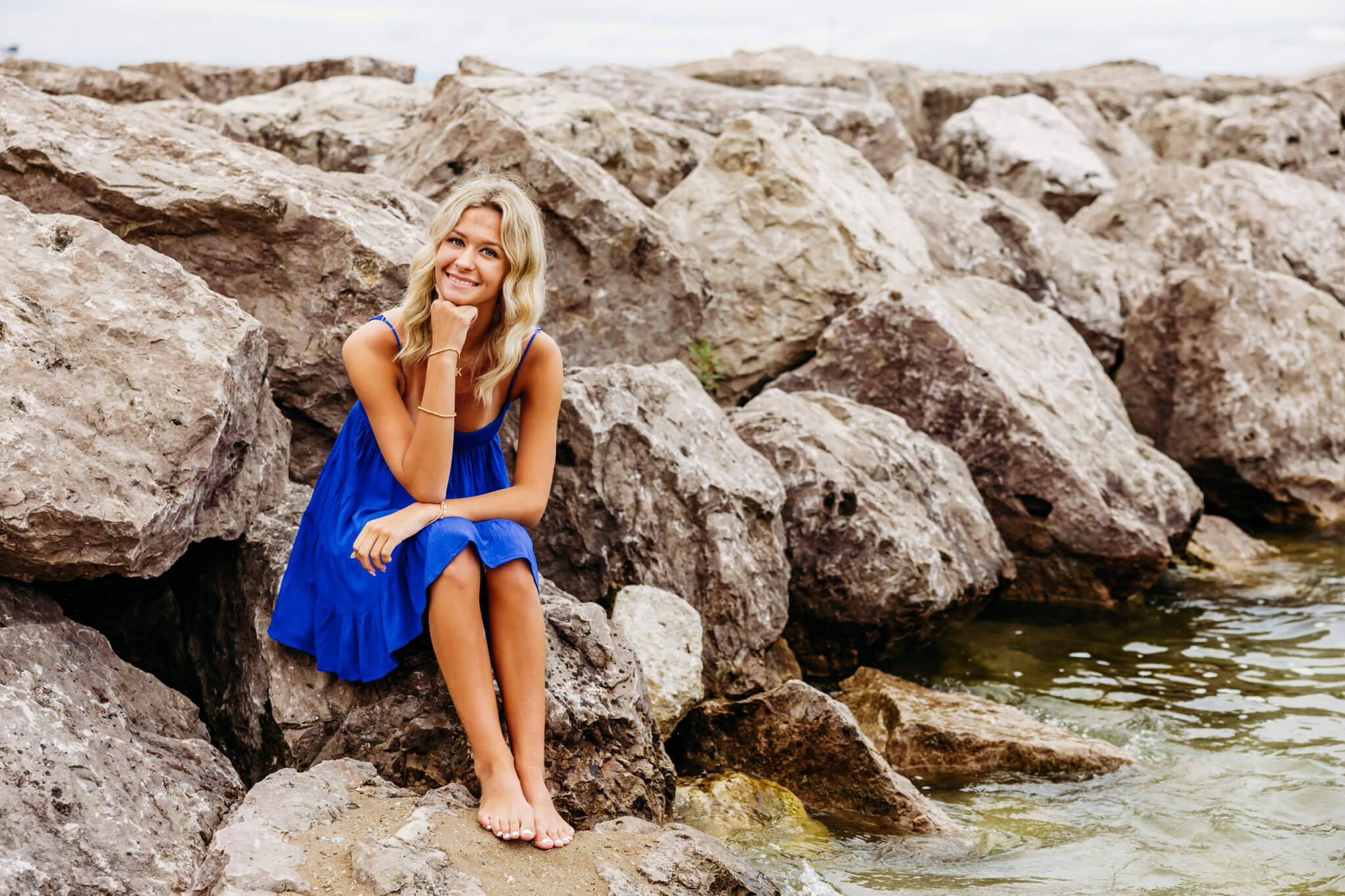 High school senior girl sitting on some large rocks along the edge of the beach in Egg Harbor.