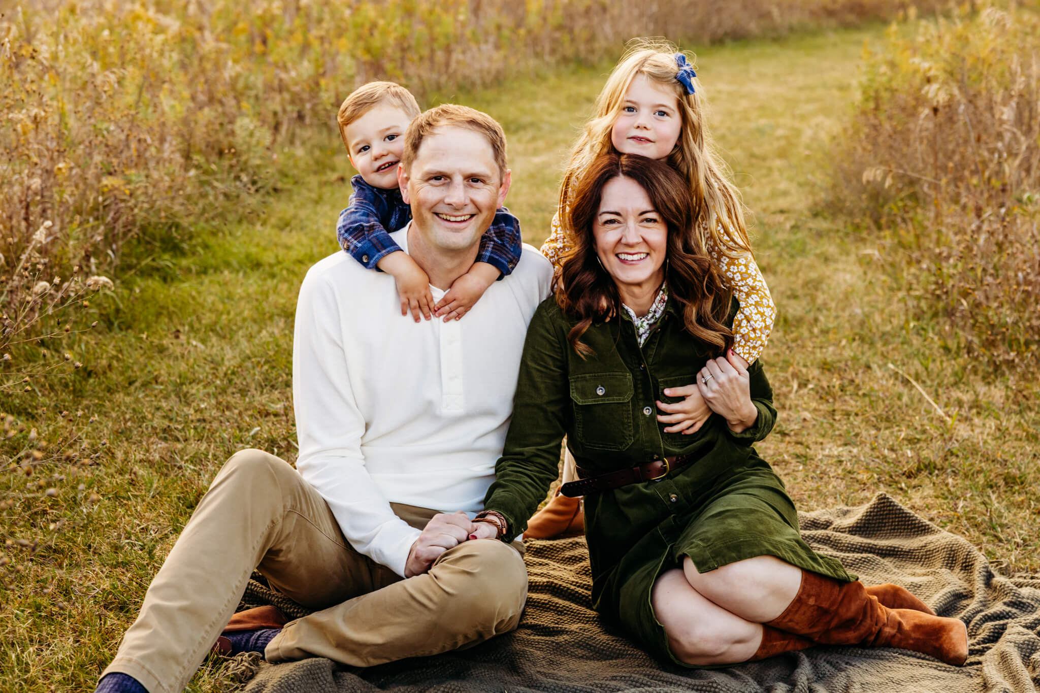 Mother and father sitting on the grass with their two young children and everyone laughing together.