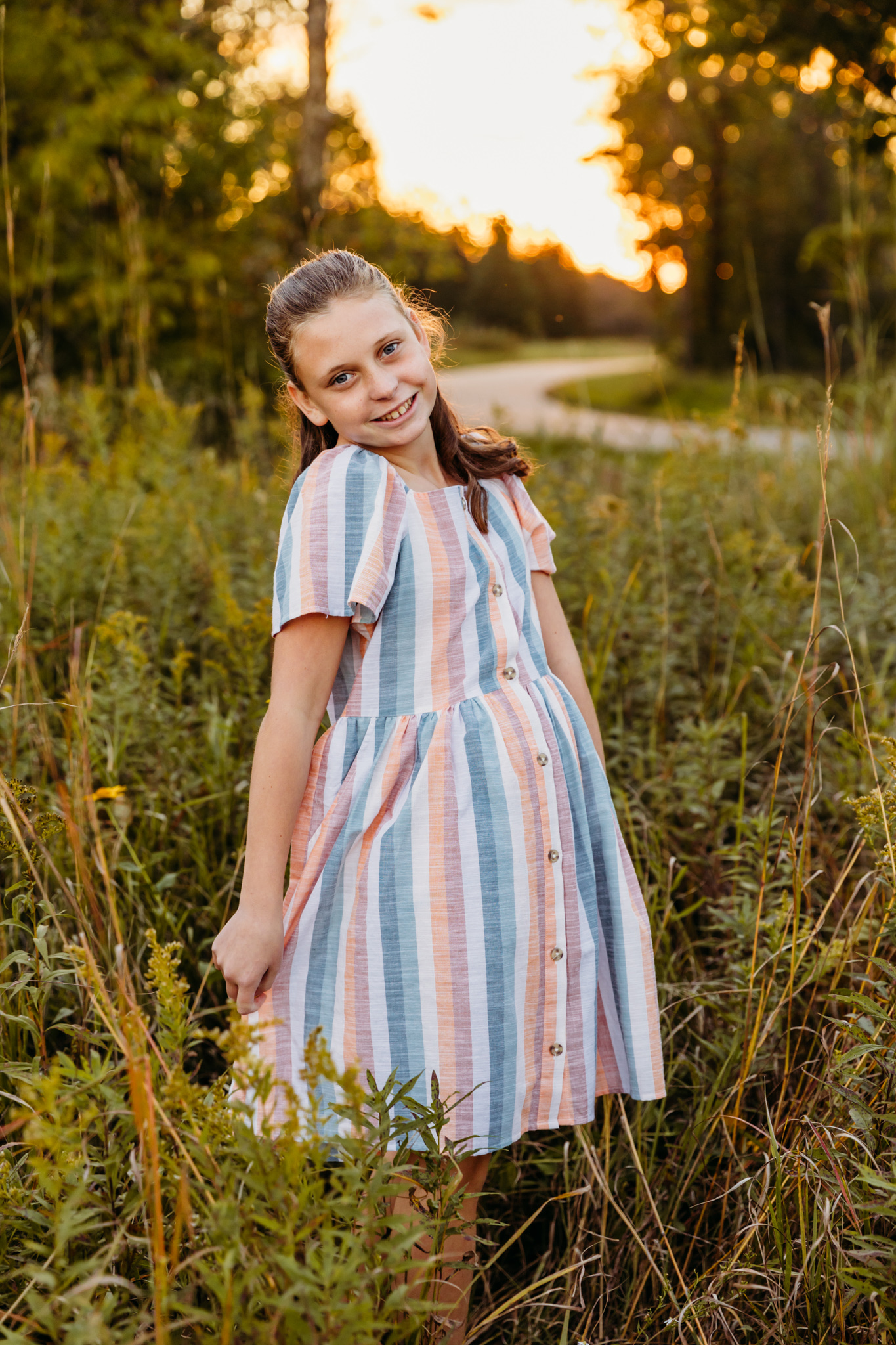 A young girl stands in a tall grass park field at sunset while twirling her striped colorful dress things to do in Fond du lac
