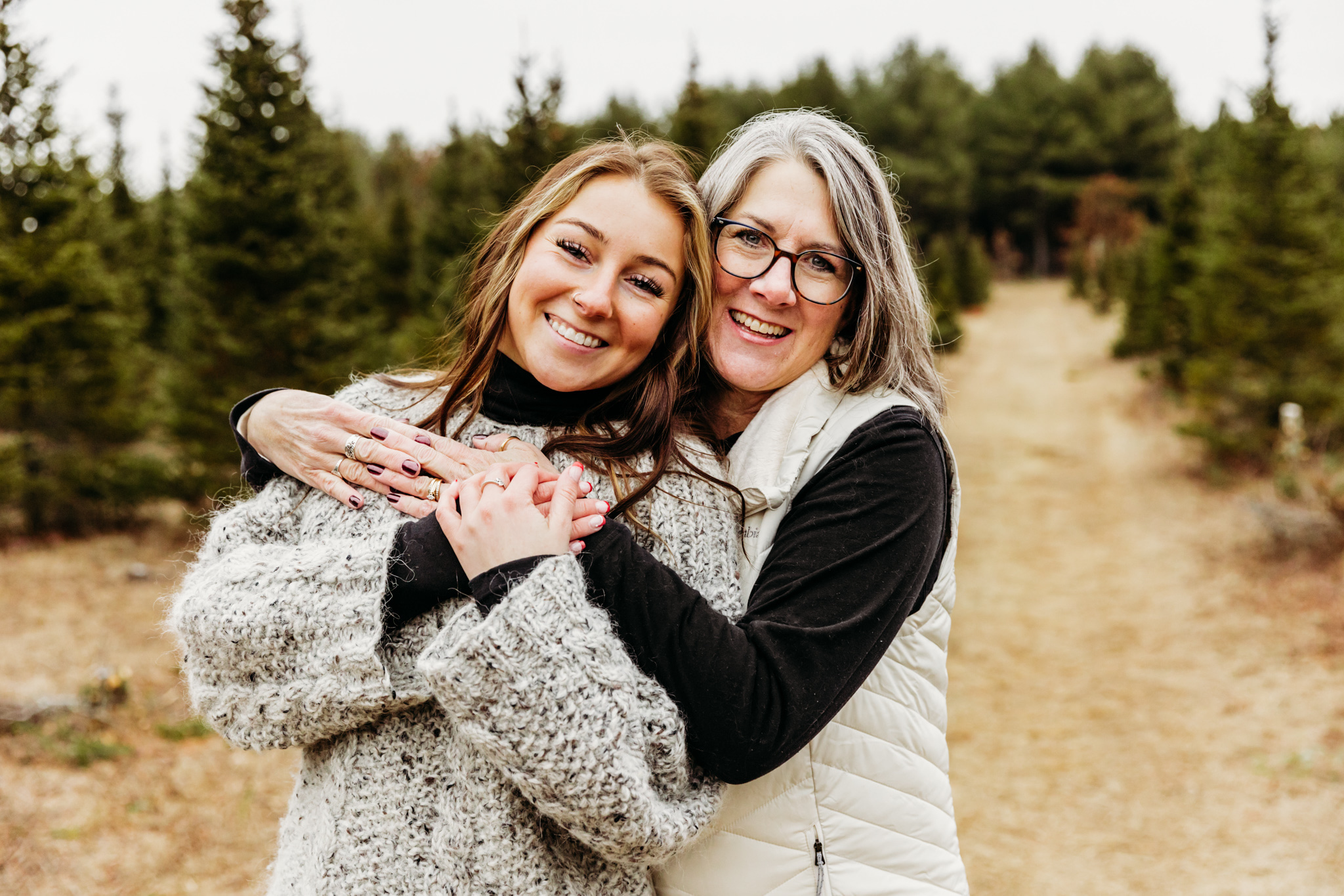 A mother hugs onto her teenage daughter on a path in a christmas tree farm