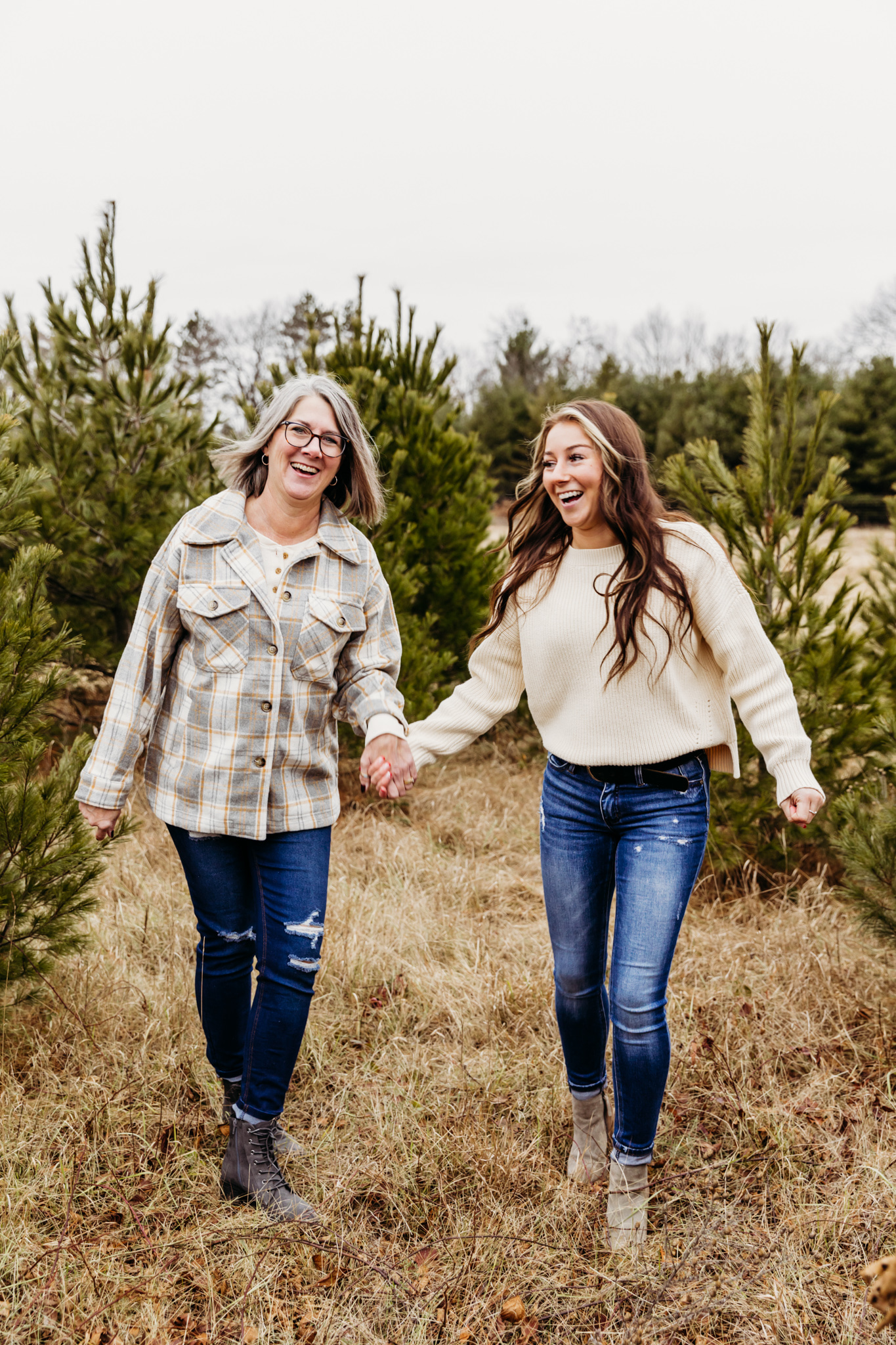 Mother and daughter walk and play in blue jeans and sweaters in a christmas tree farm Thornberry Cottage