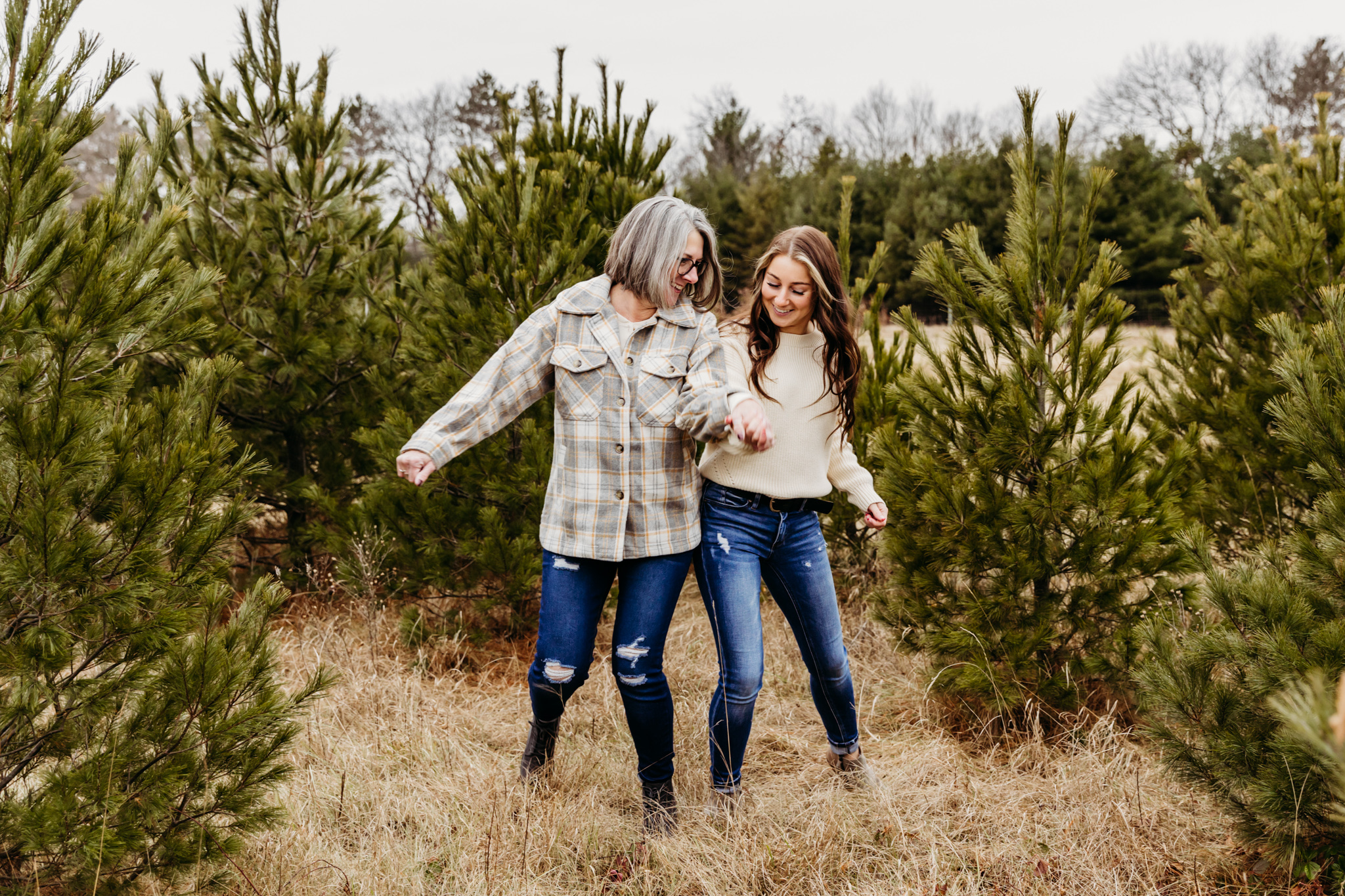 A mother and daughter bump hips together wearing blue jeans in a christmas tree farm Thornberry Cottage