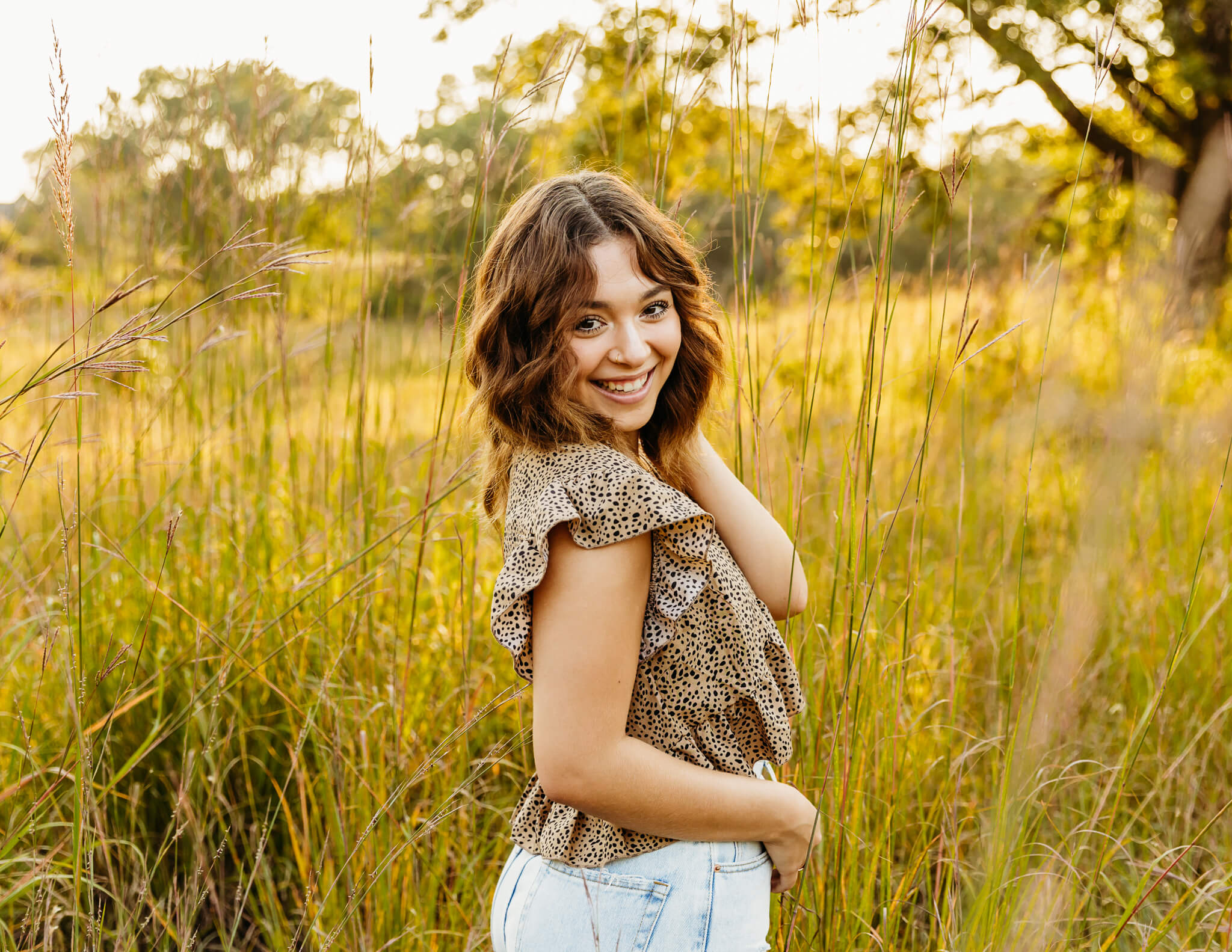 gorgeous high school girl looking back over her shoulder while standing in a glowing field of grass