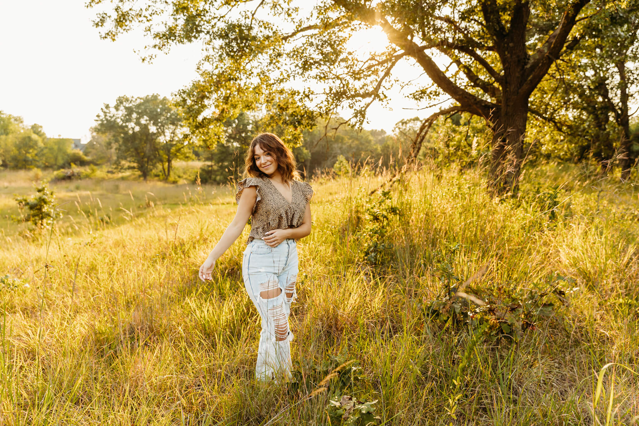 high school senior girl in a brown top and jeans walking in a field near Oshkosh by Ashley Kalbus Photography
