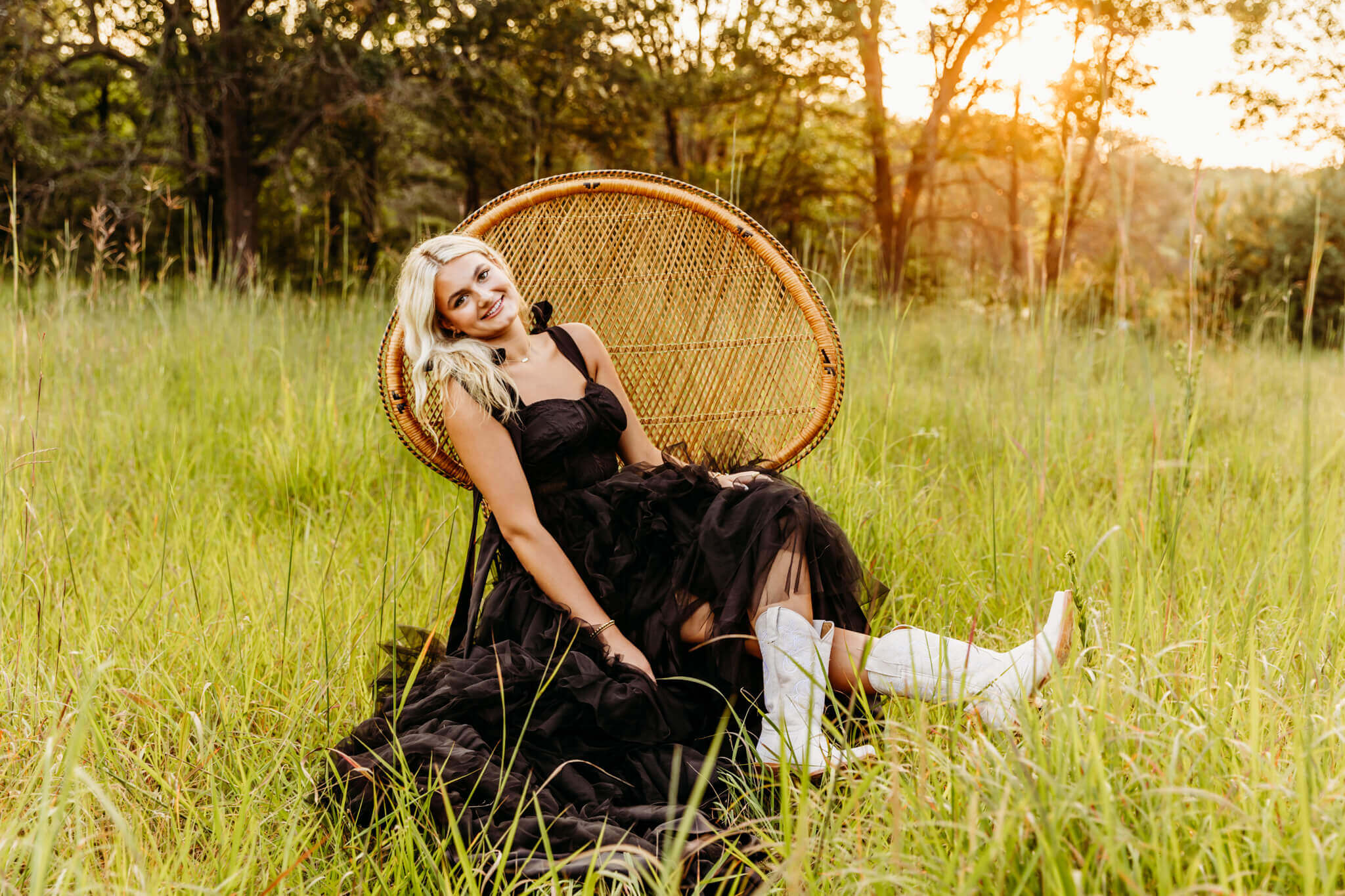 pretty teen girl in a black ball gown wearing cowboy boots sitting on a peacock chair in a grassy field.