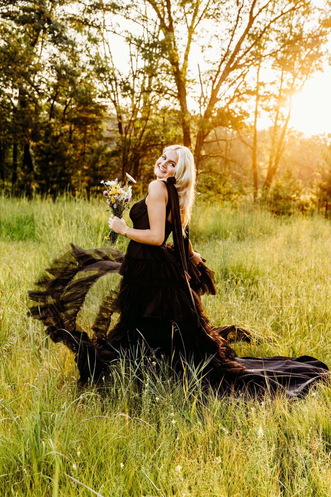 beautiful teenage girl from Lourdes Academy Oshkosh in a black gown holding a bouquet of flowers spinning for her senior photo session