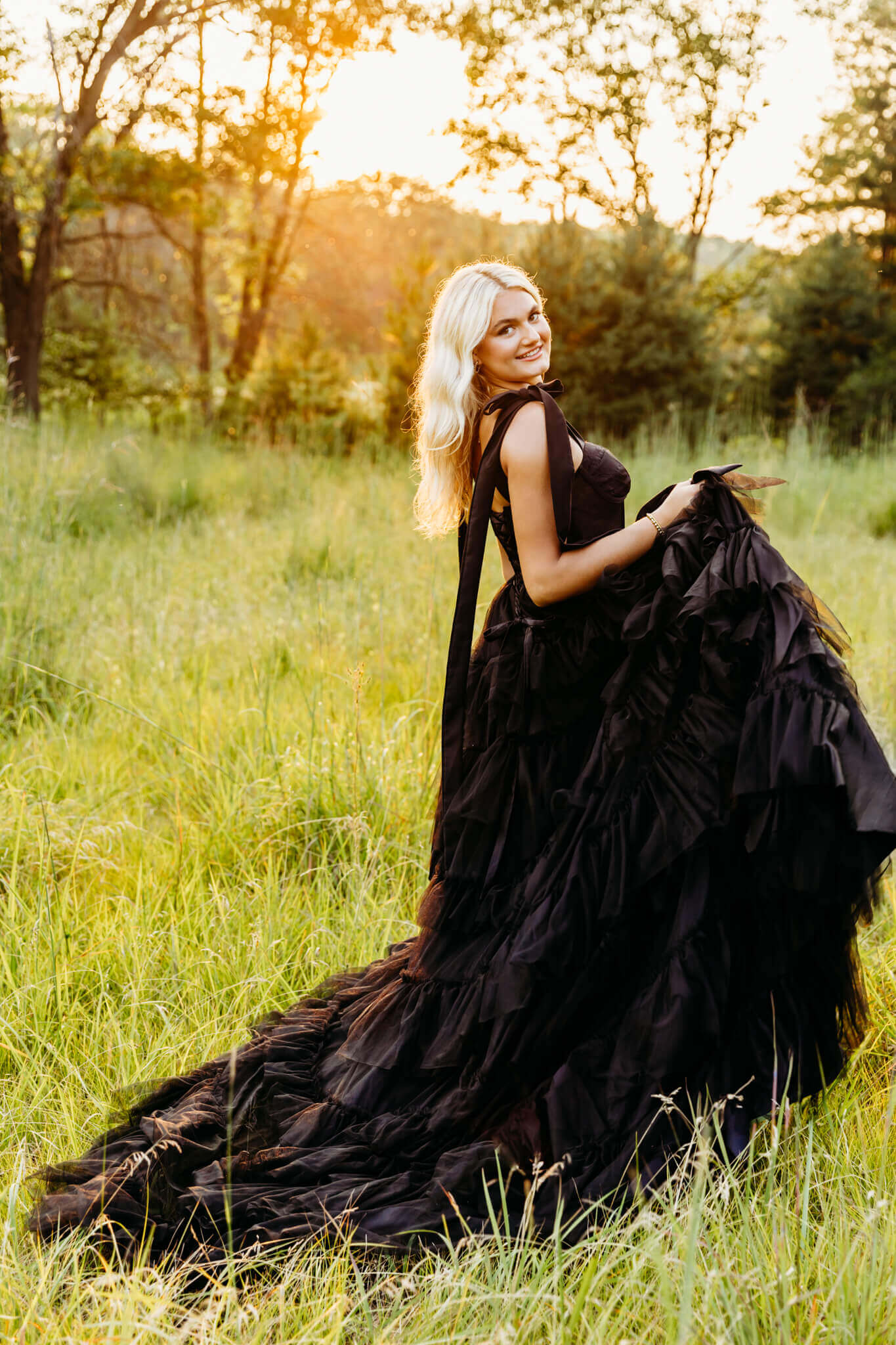 young lady in a stunning black gown playing with her dress at sunset 