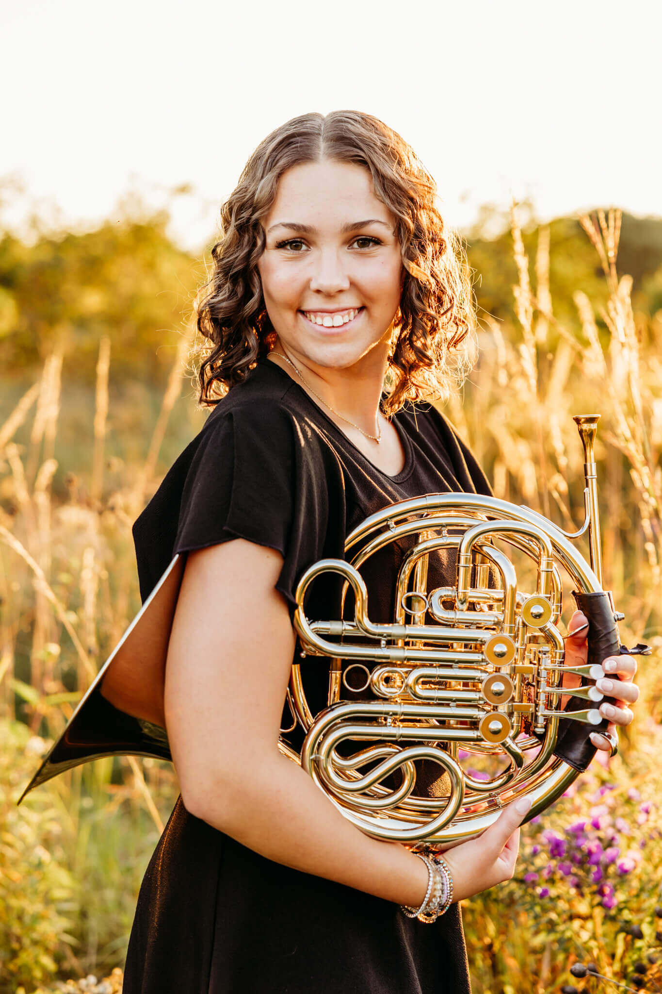 teenage girl in a black dress holding her french horn for her senior portraits