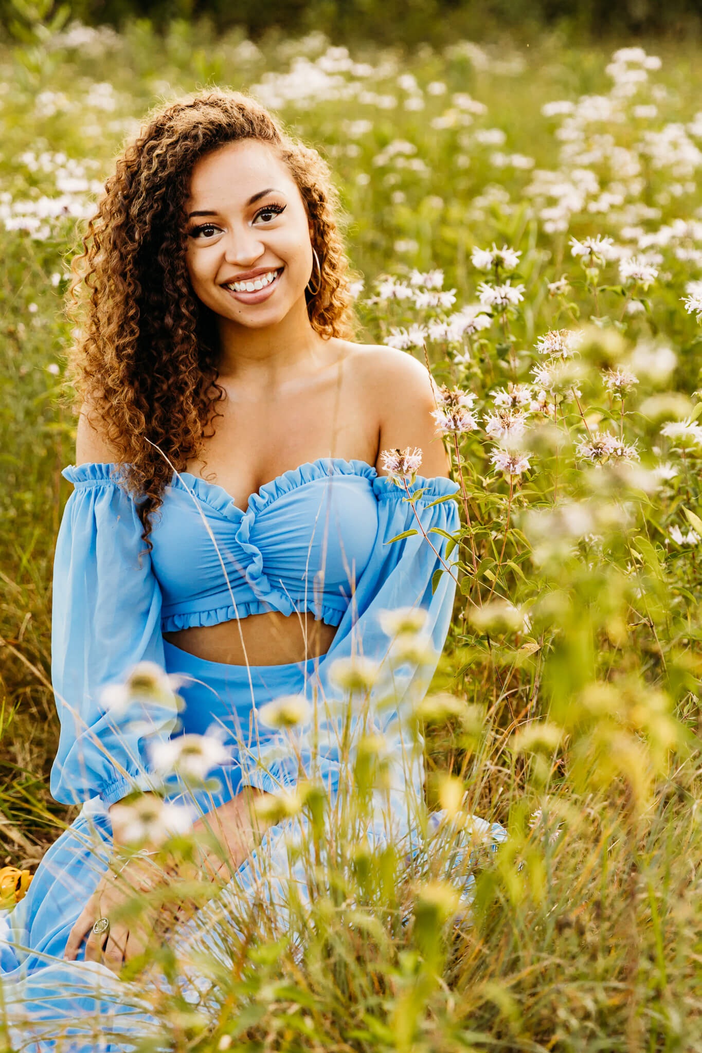 beautiful teen girl sitting in a field of wildflowers in a blue dress for her high school senior session 