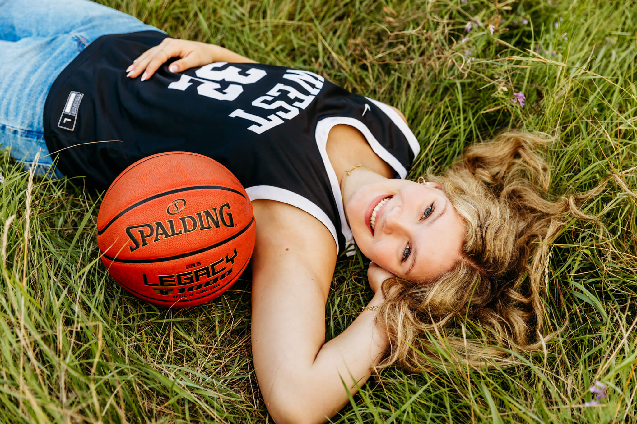 young lady in a high school basketball jersey laying on her back next to a basketball and looking up