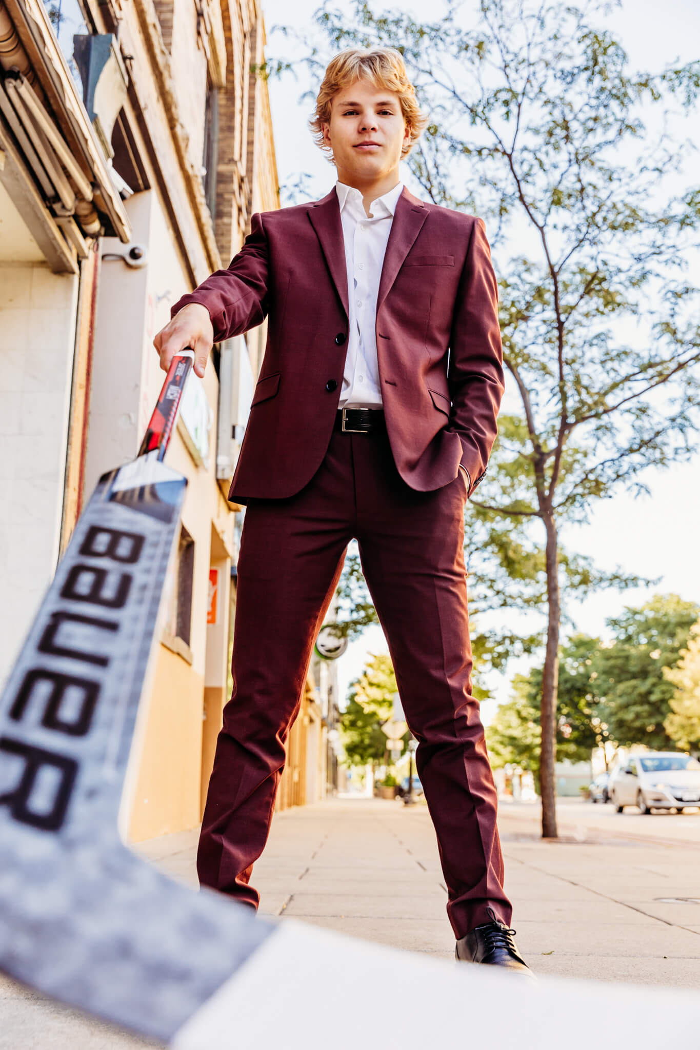 teen boy in a burgundy suit looking down as he holds his hockey stick out