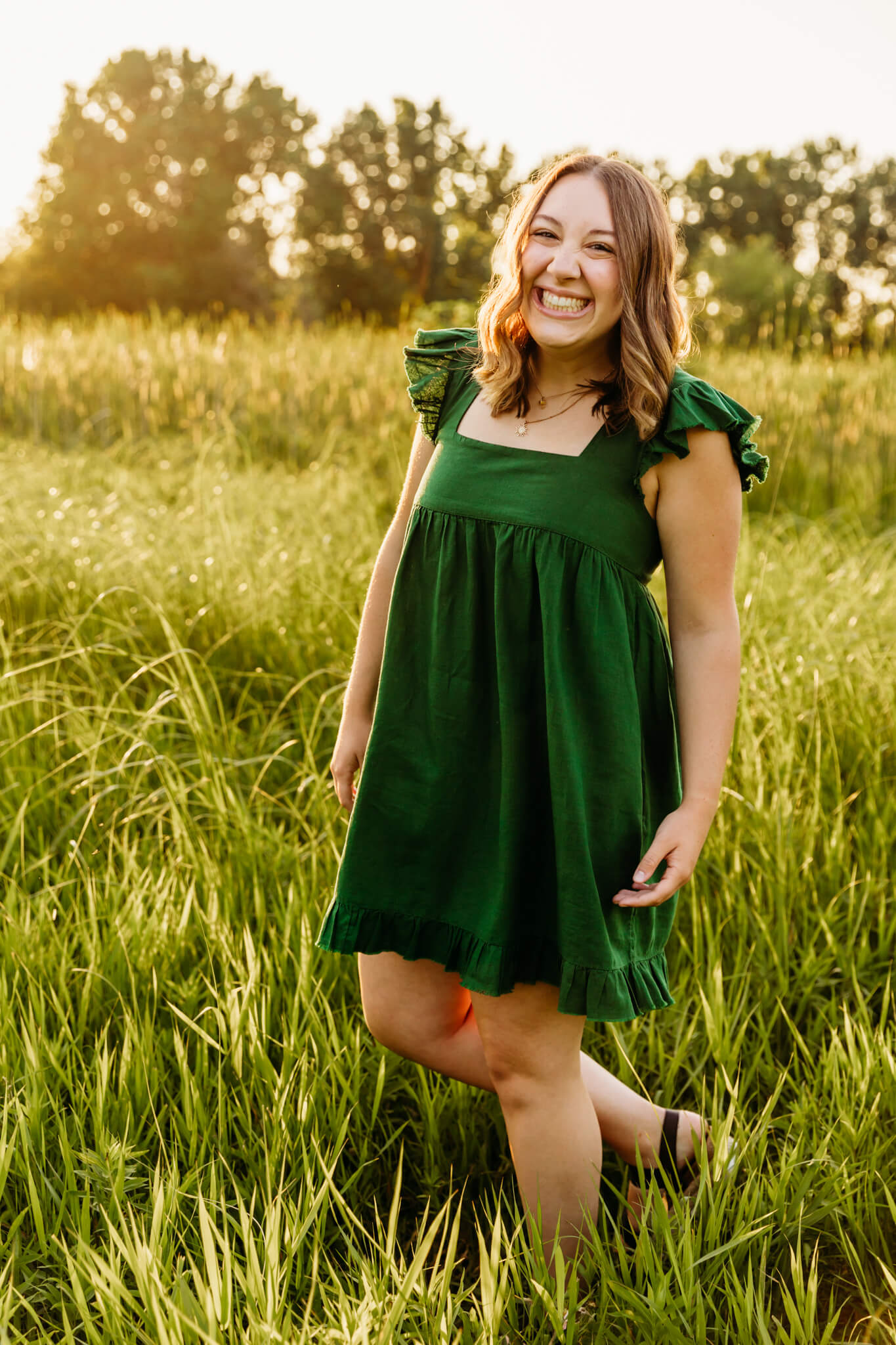 beautiful high school senior girl walking through a grassy field at sunset for senior photo session
