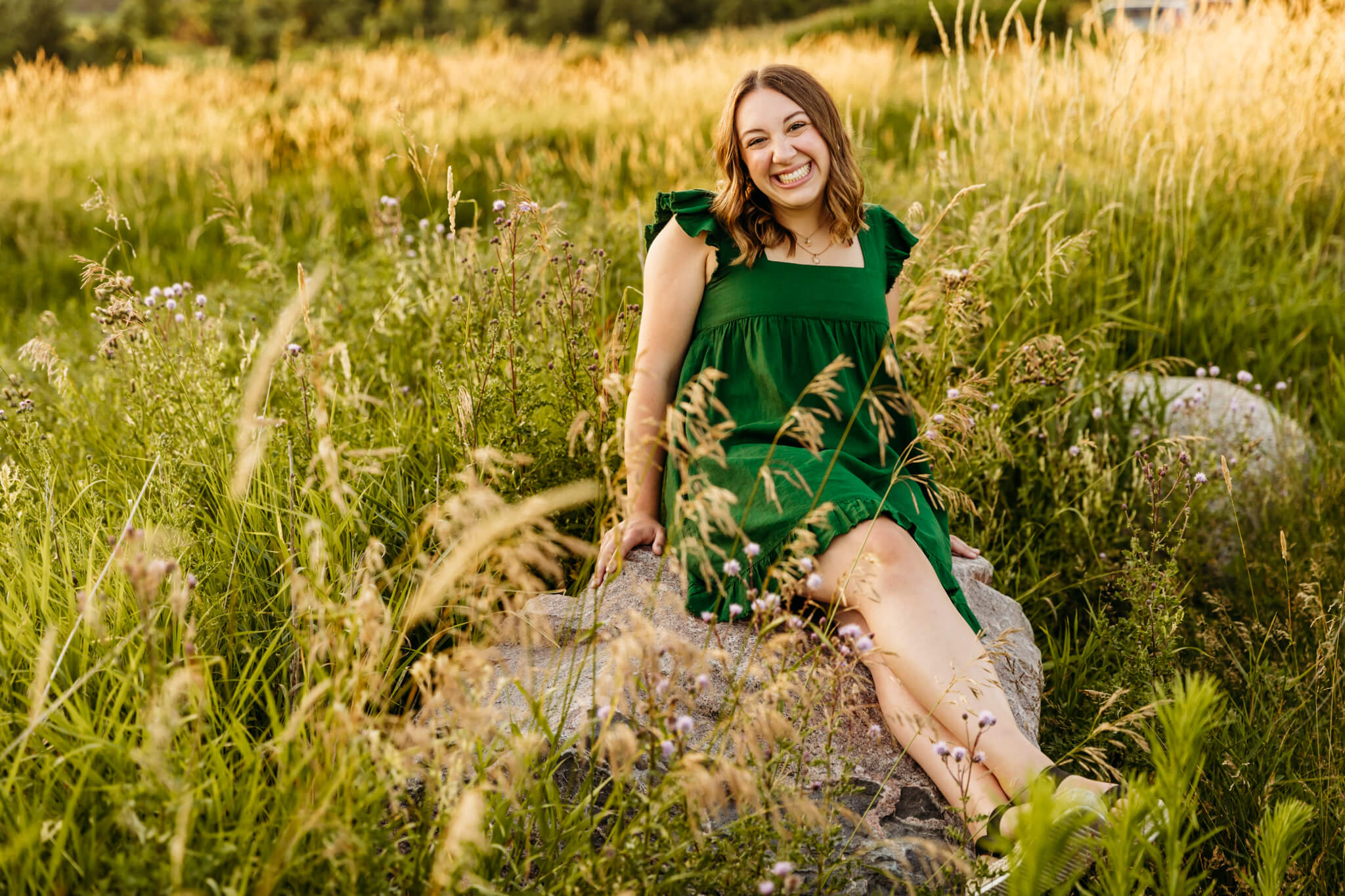 stunning teen woman in a green dress sitting on a rock, smiling for the camera for blog about providence academy green bay